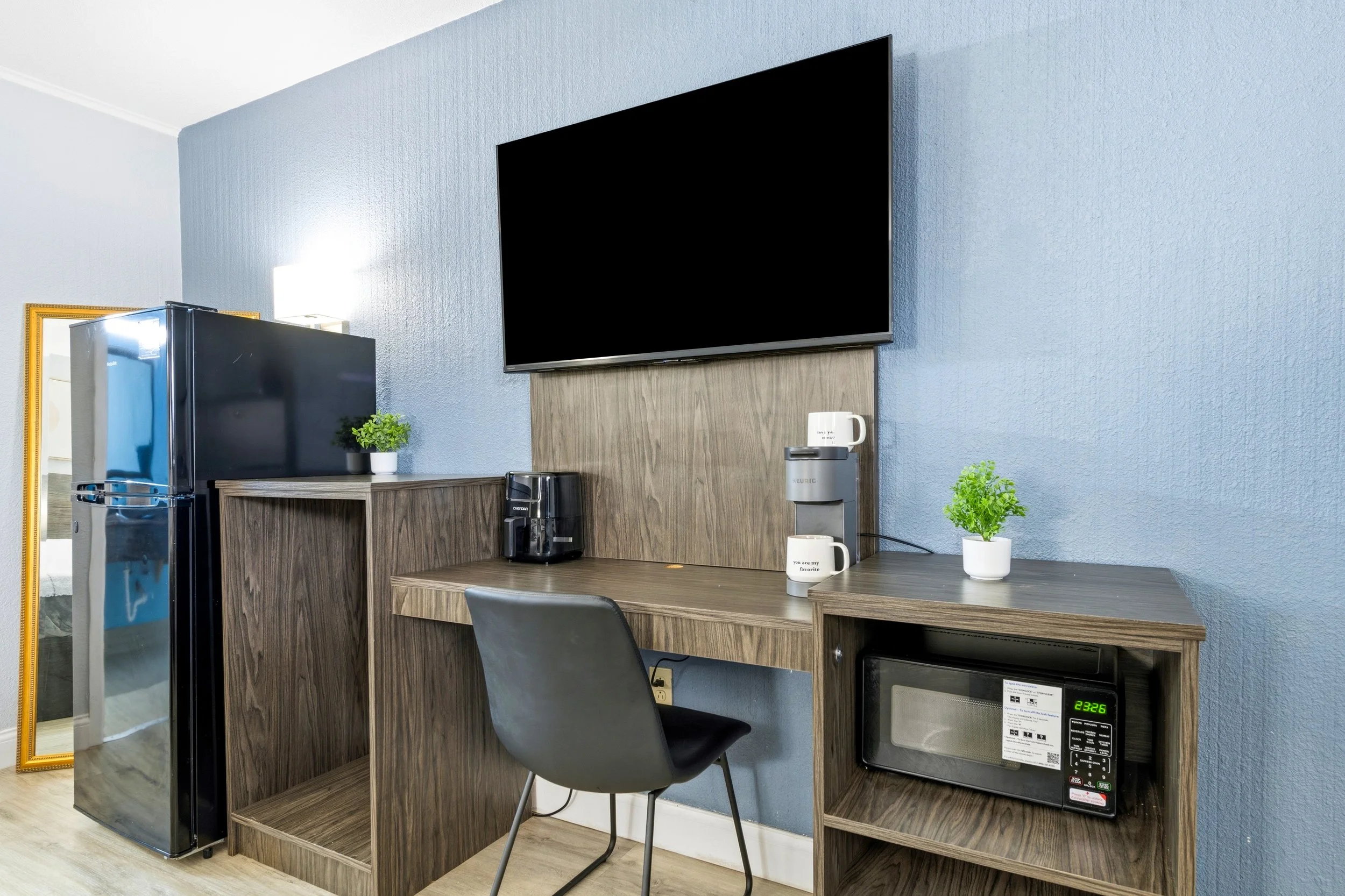 A kitchenette with a black refrigerator, a microwave oven, a coffee machine, and potted plants on a wood countertop setup.