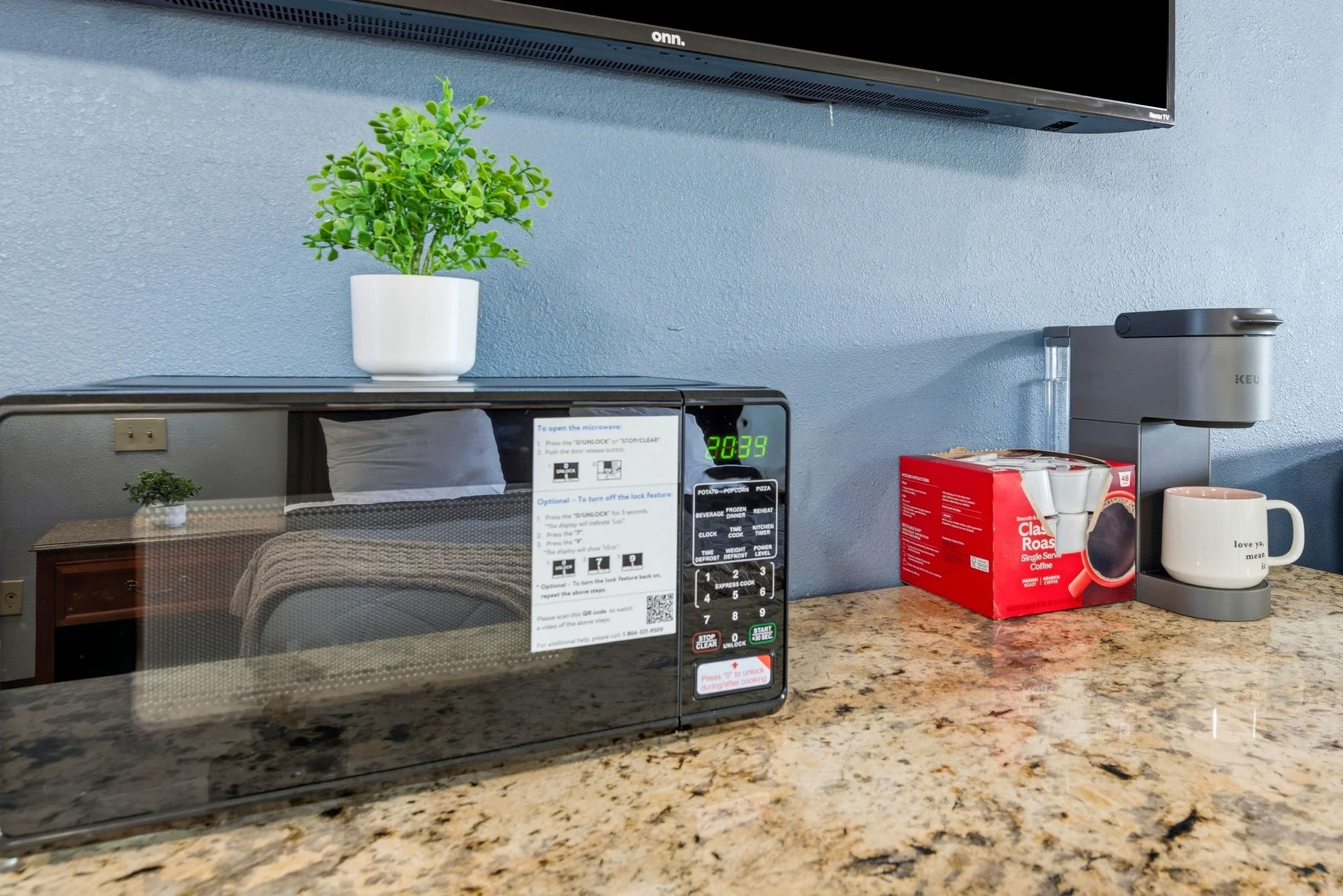 A kitchen countertop with a microwave oven, a potted plant, a box of coffee, and a coffee maker mounted on the wall above.