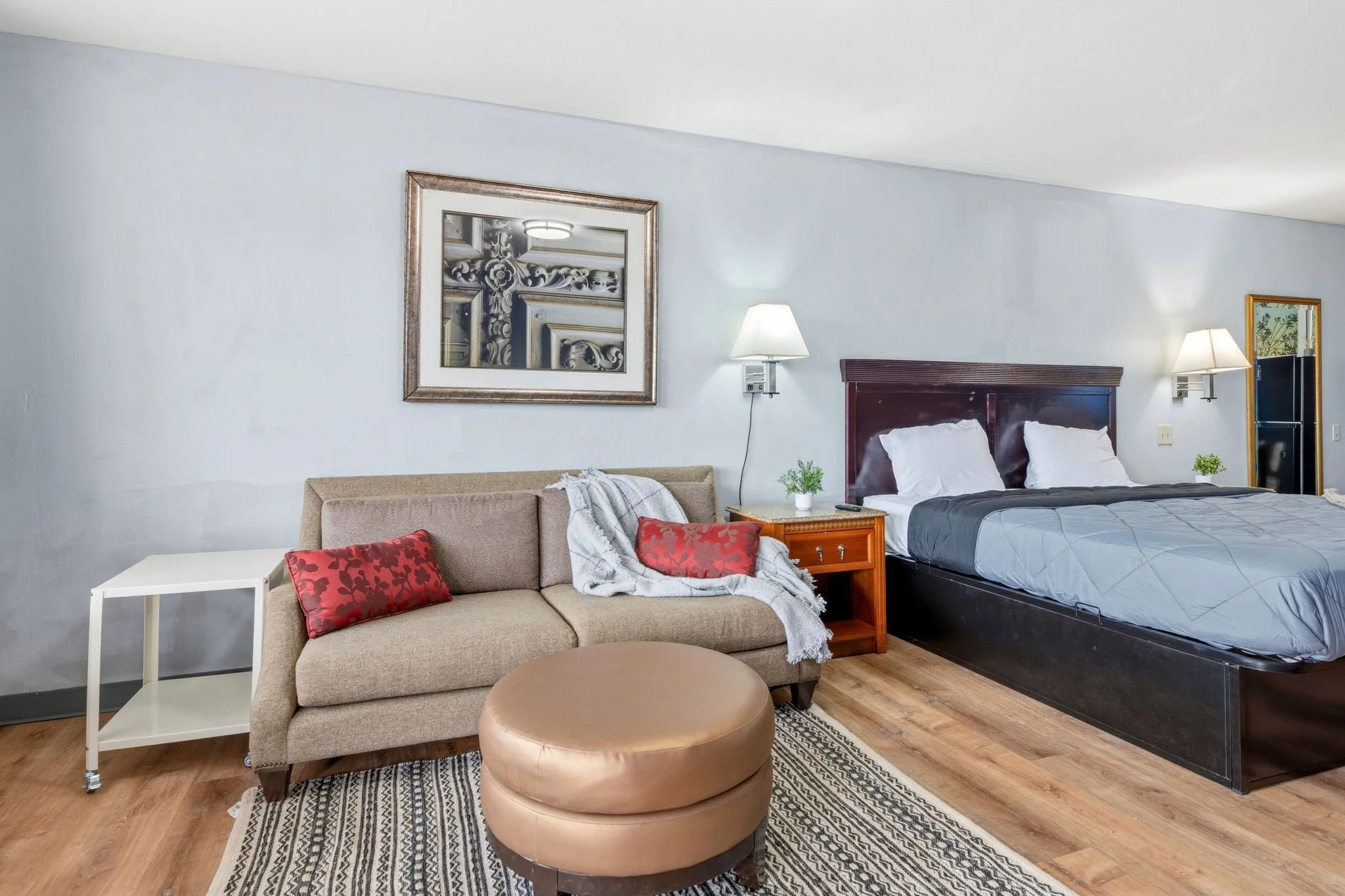 A hotel room with a bed, bedside lamps, a sofa with red pillows, a small table, and artwork on the walls.
