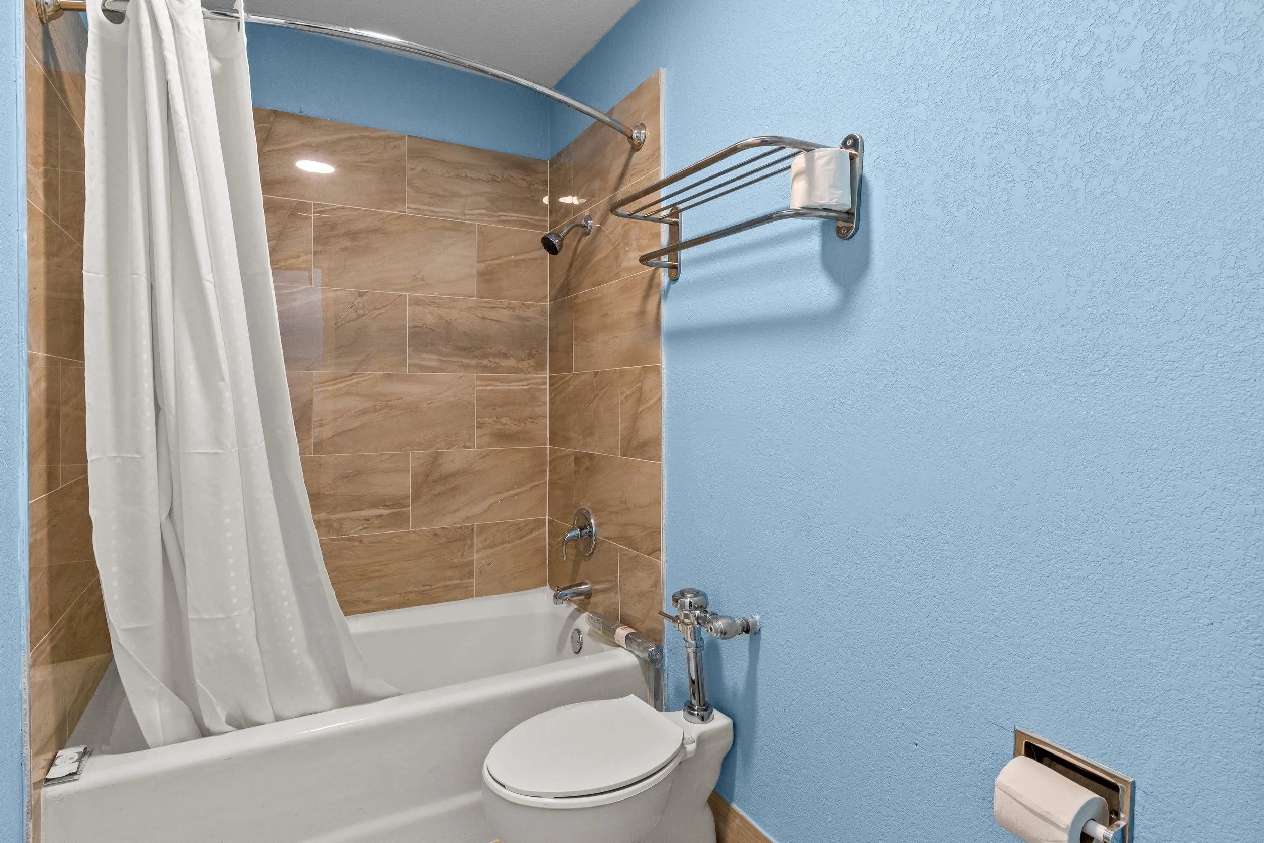 Bathroom with bathtub, shower curtain, light brown tiled wall, blue painted wall, and a toilet with a closed lid.