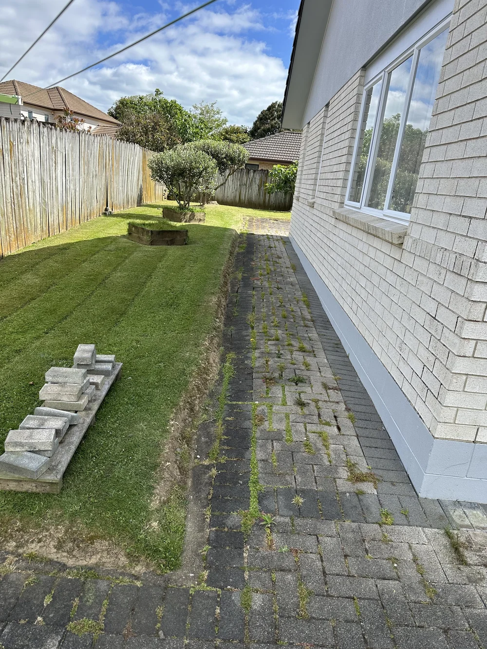 Overgrown paving path beside a Golflands home with weeds growing through large gaps between pavers
