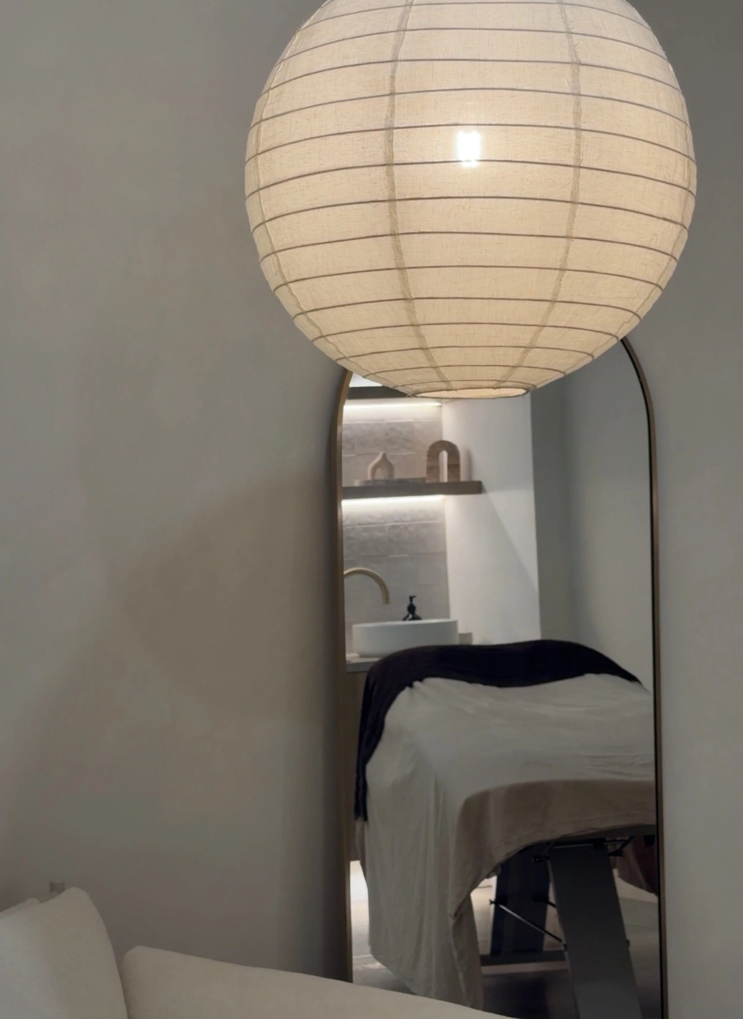 Shot through a curved mirror with a linen lamp in front, looking at the brow room bed and sink set up.