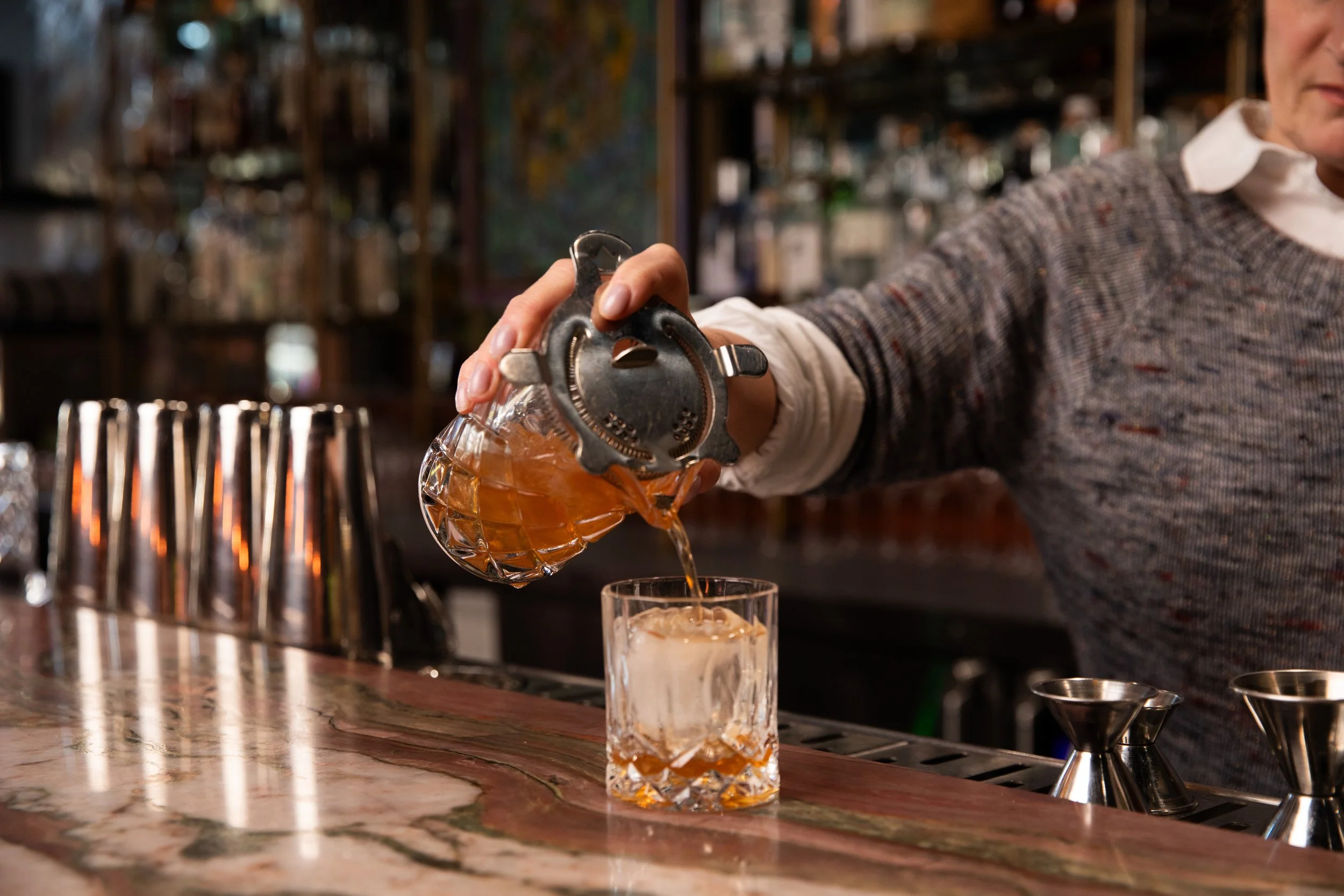 Bartender pouring an old fashioned over a large cube
