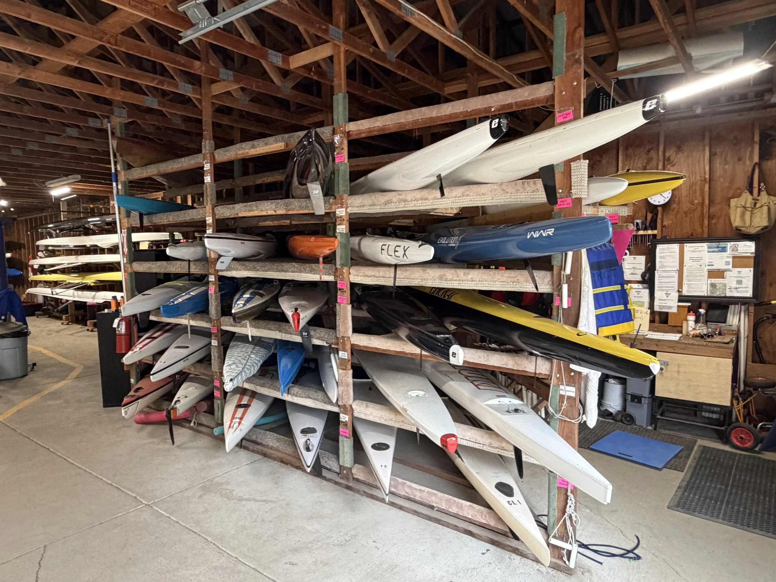 Wooden storage rack holding multiple kayaks and paddleboards in a warehouse