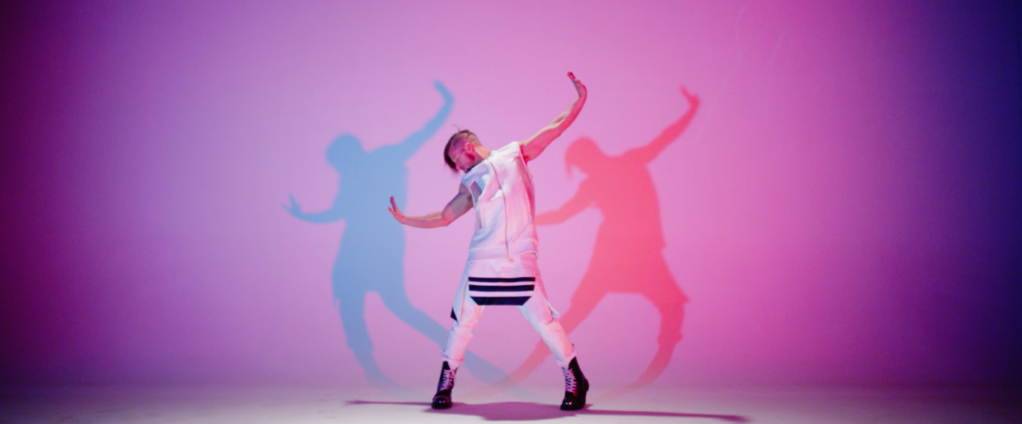 Person dancing in front of a pink and purple background with colorful shadows.