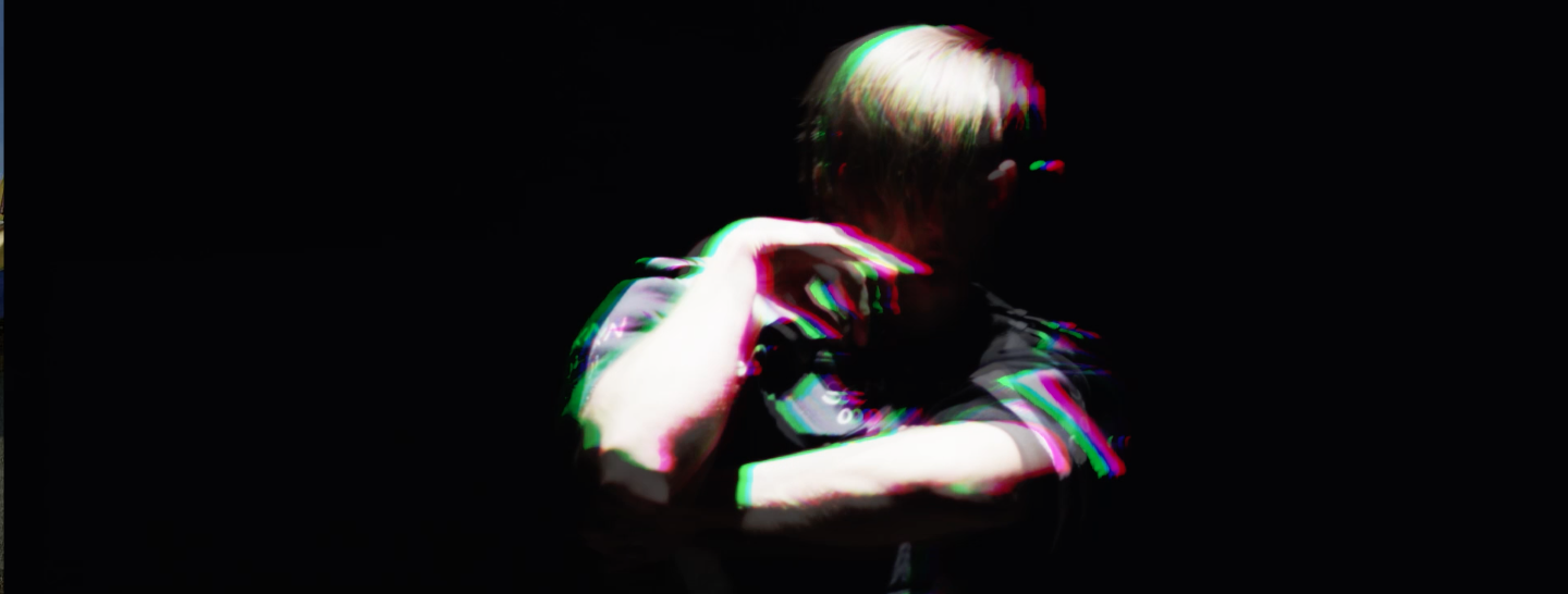 Person with light-colored hair adjusting glasses, wearing a dark shirt, in a dark environment with a glitch effect