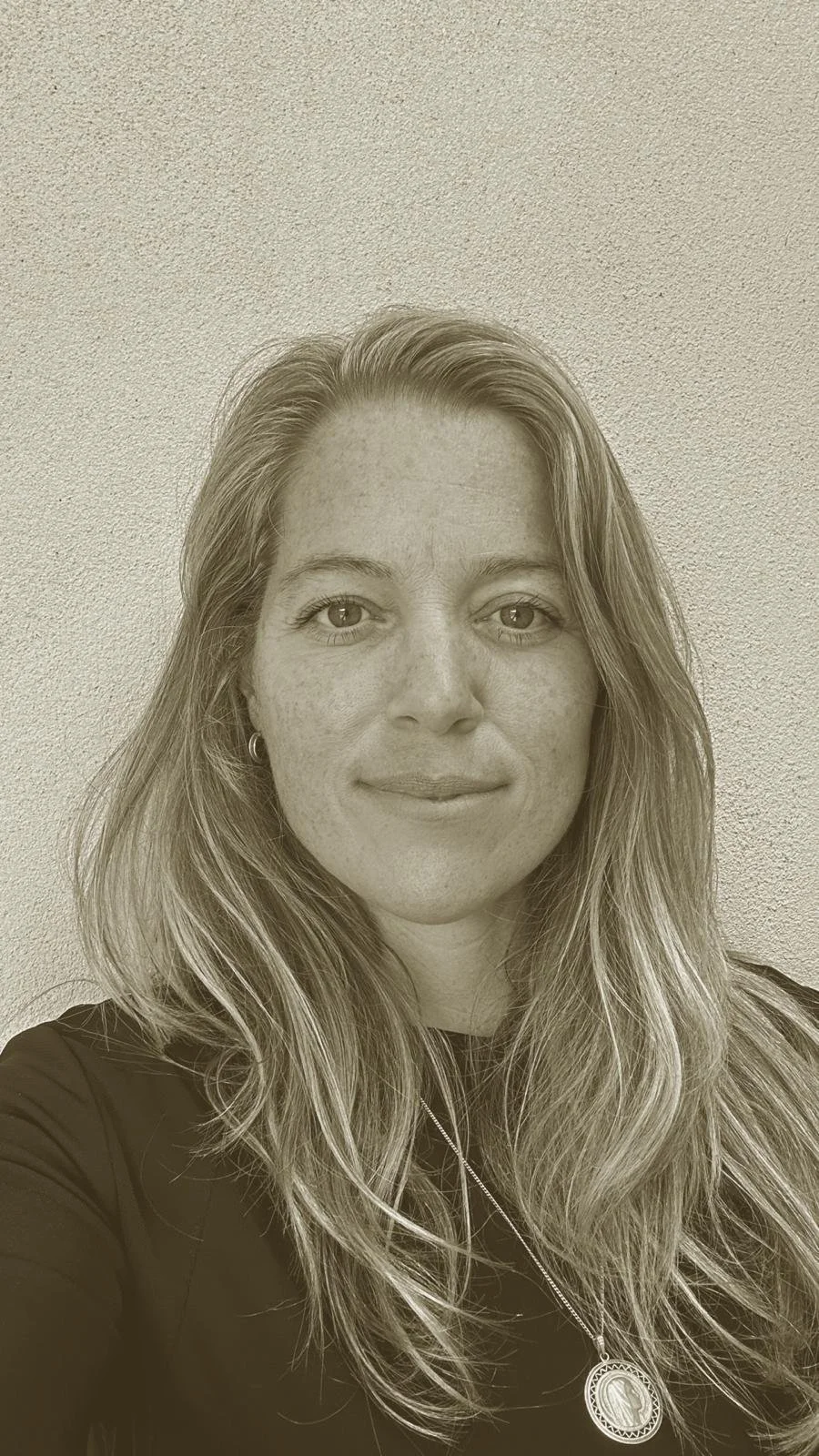 Sepia-toned portrait of a woman with long hair, wearing a necklace, in front of a neutral background.