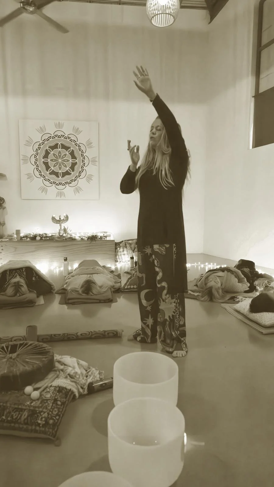 Woman performing sound healing session with crystal singing bowls and people lying on the ground