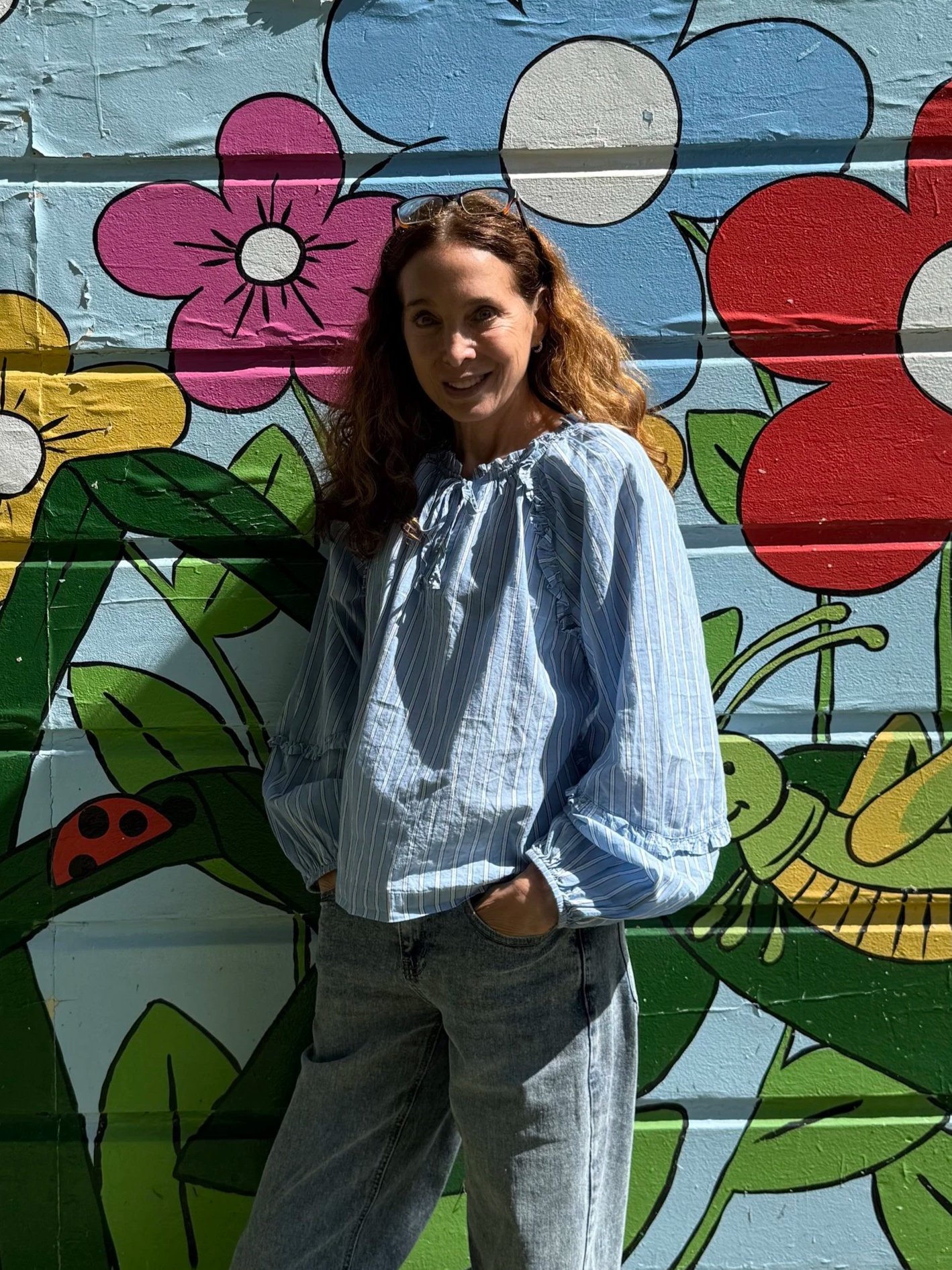 Teacher standing in front of a colorful mural with floral designs.