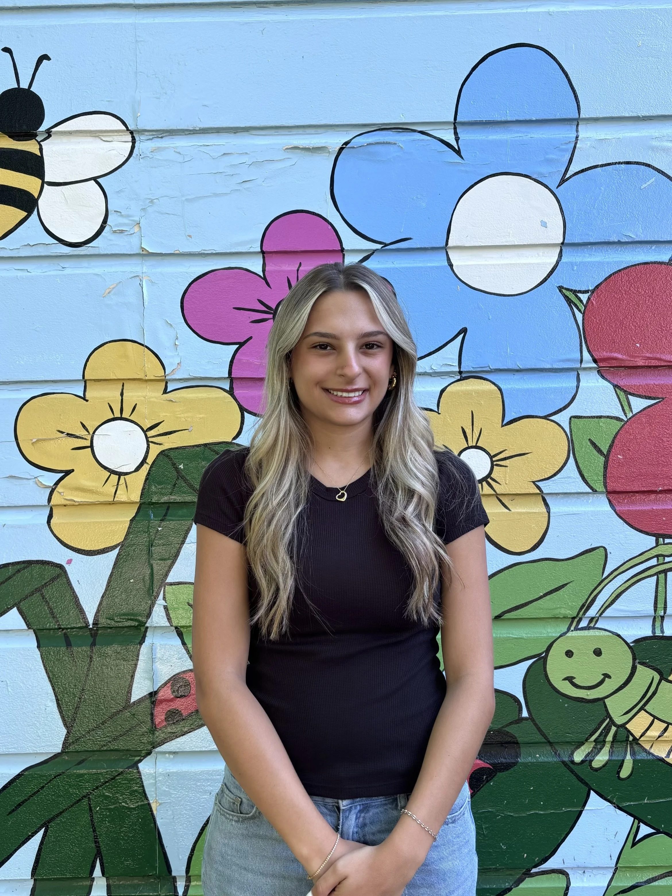 Teacher standing in front of a colorful mural with floral designs.