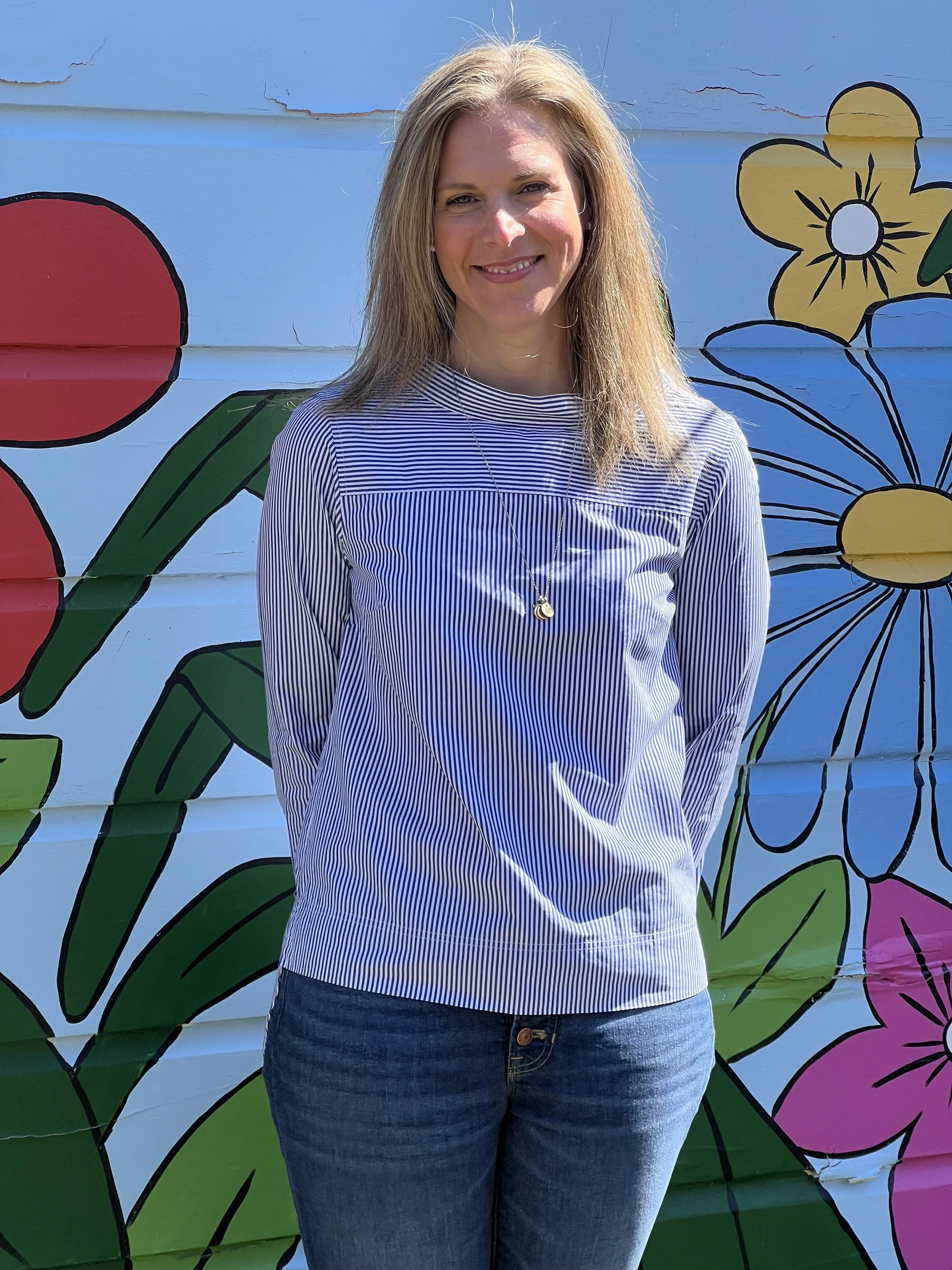 Teacher standing in front of a colorful mural with floral designs.
