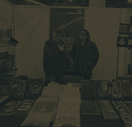 Dos personas en un puesto de cómics y arte alternativo, con posters y libros en exhibición.