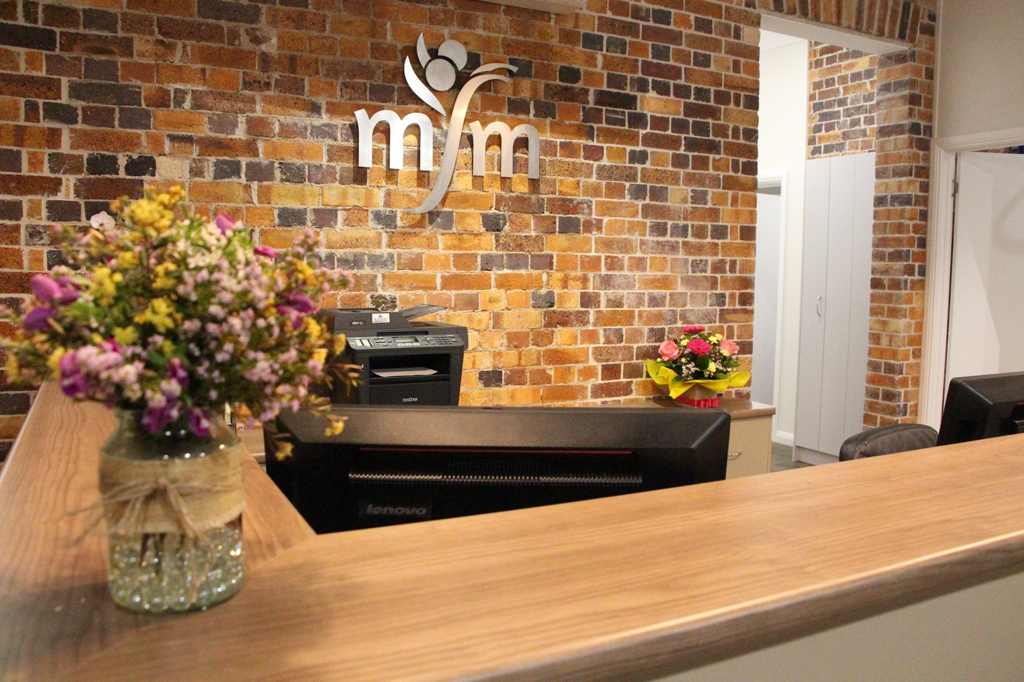 Interior of an office with a brick wall, flower arrangements on the desk, a telephone, and a logo on the wall behind the desk.