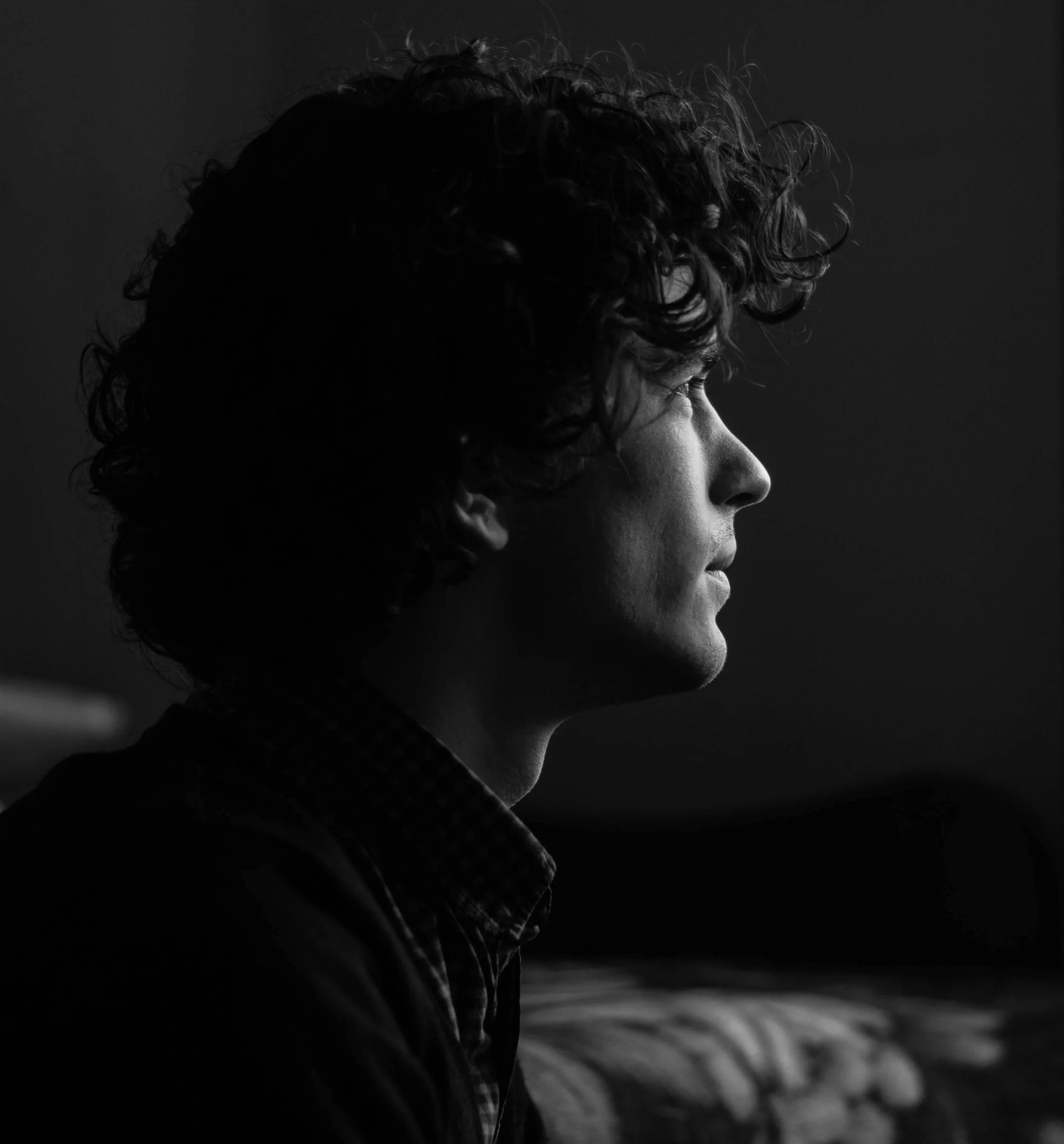 Black and white side profile of a man with curly hair looking thoughtfully into the distance.