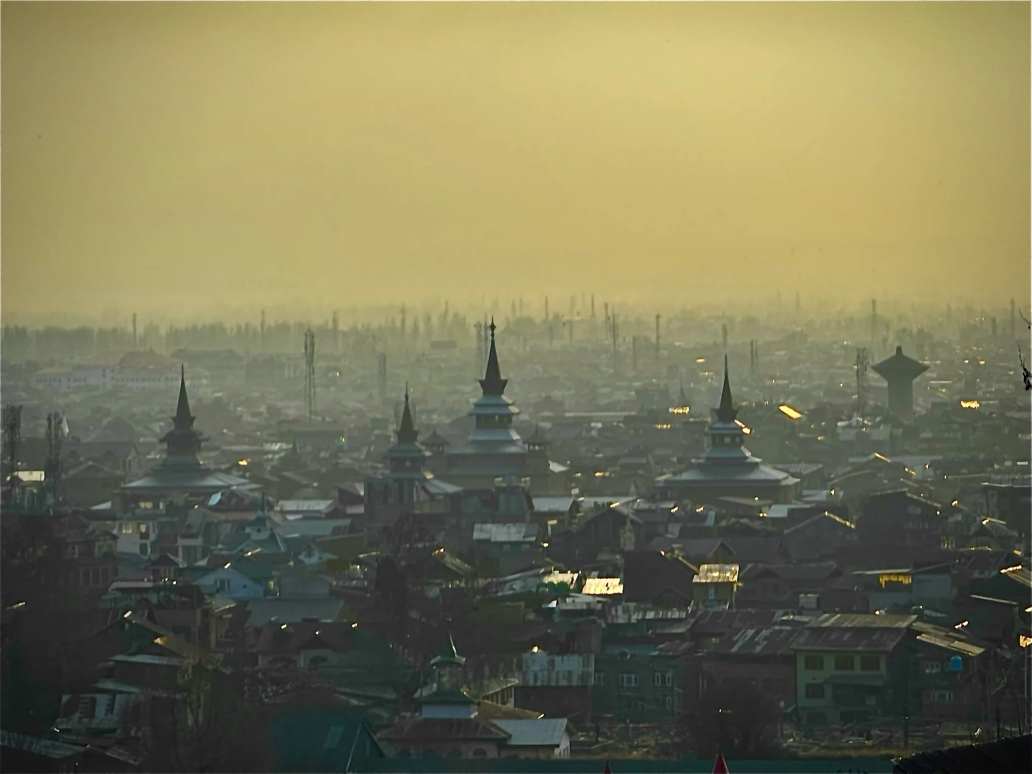 A cityscape with multiple church steeples and rooftops, set against a hazy, yellowish sky.