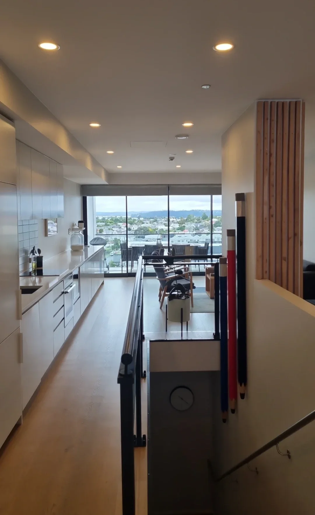 Modern apartment interior with a kitchen on the left, a dining area in the middle, and a living room with large windows showing a city view.
