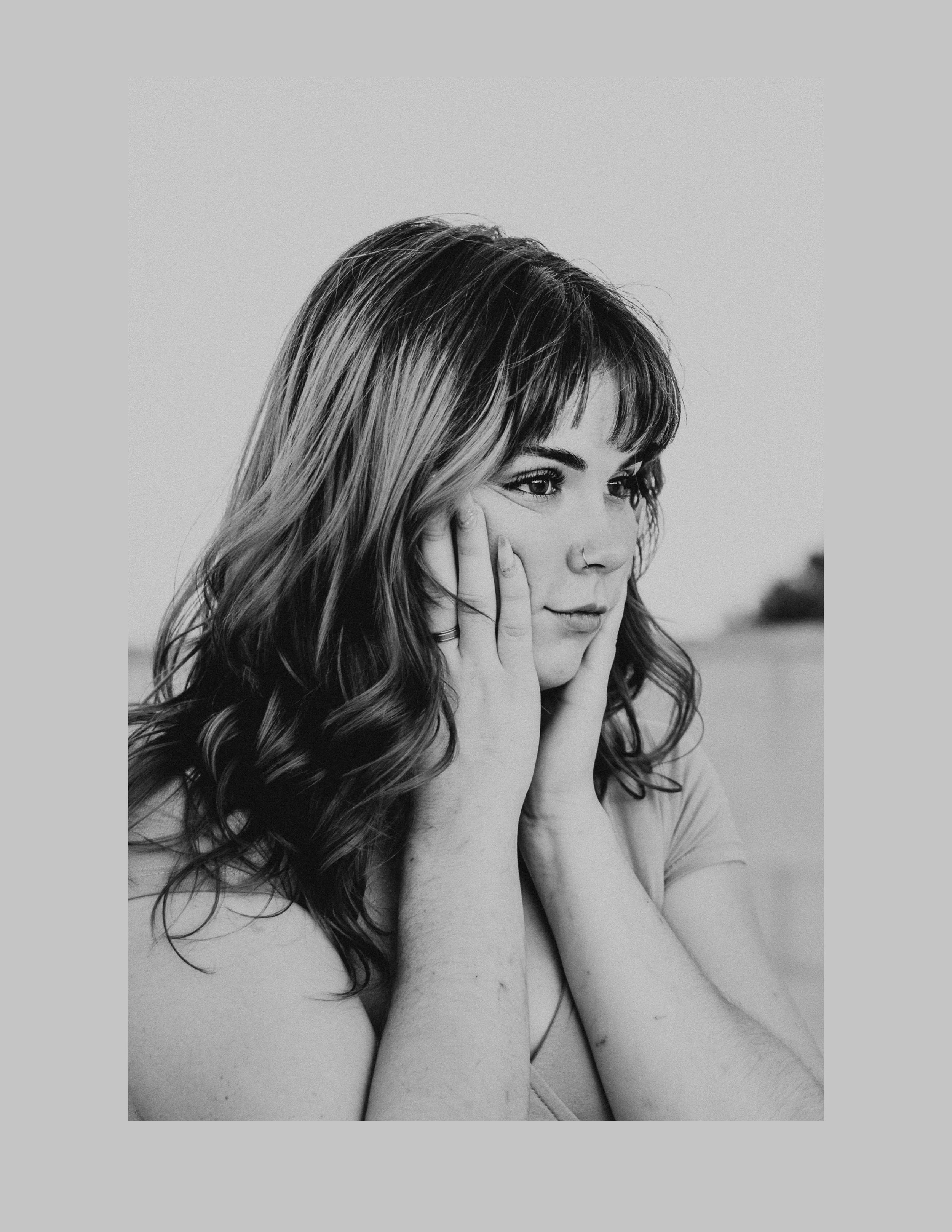Black-and-white portrait of a woman with long hair and bangs resting her face in her hands