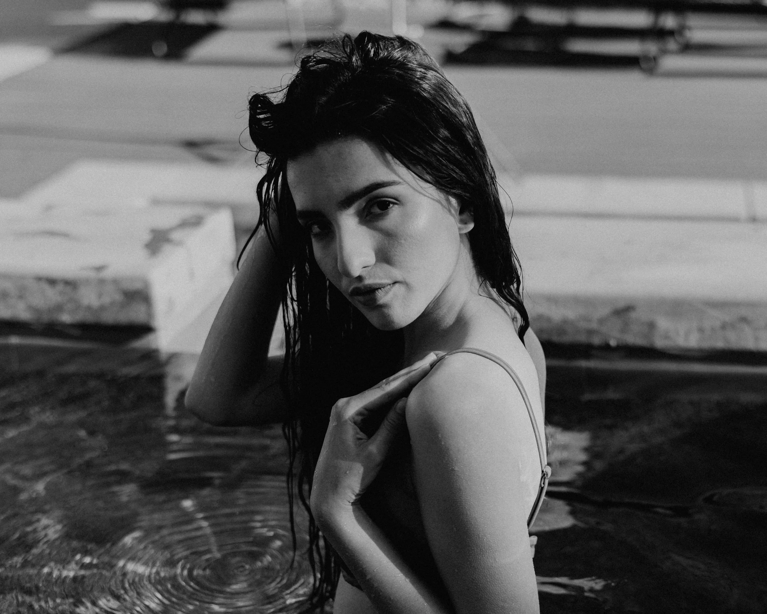 Black-and-white portrait of a woman with wet hair standing in a swimming pool