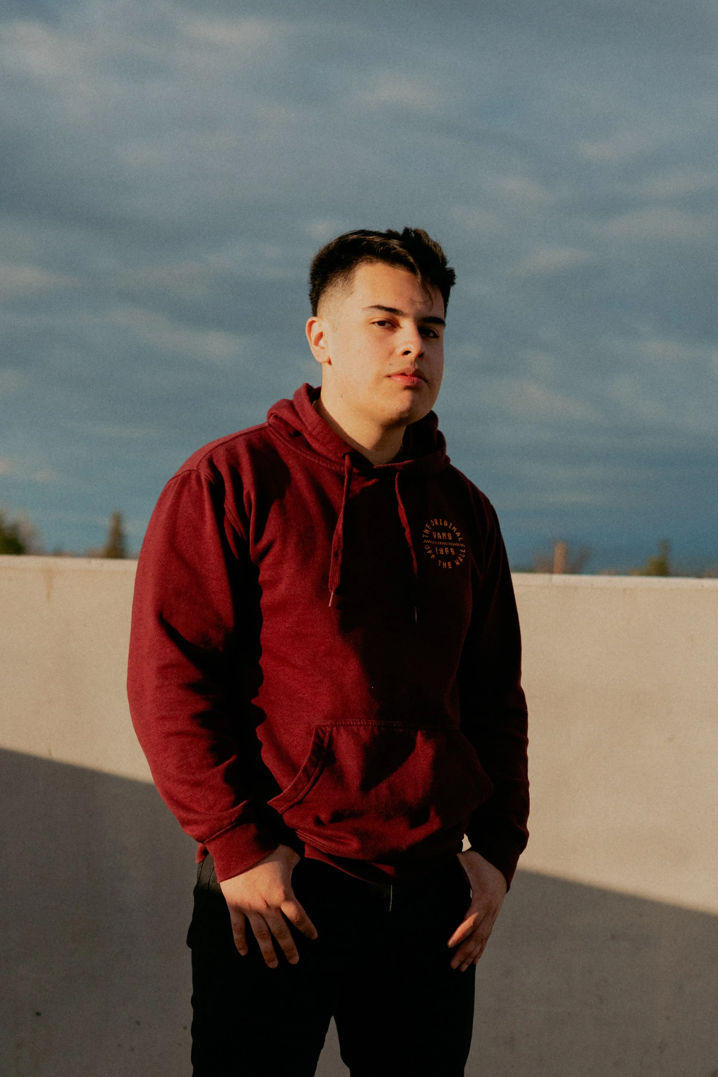 Young man in a red hoodie standing outdoors against a blue sky