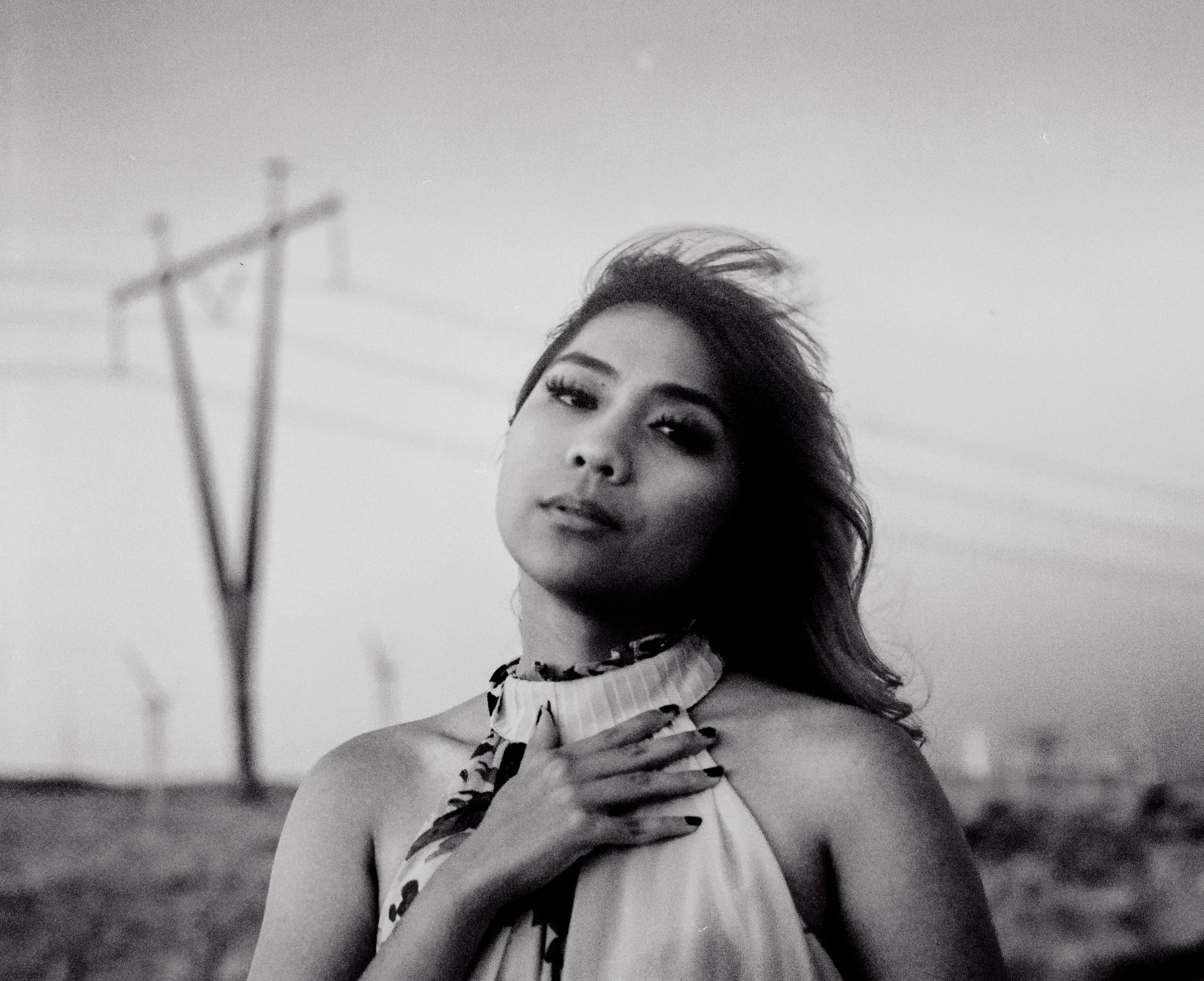 Black-and-white portrait of a woman wearing a ruffled floral blouse, gazing at the camera with one hand on her chest