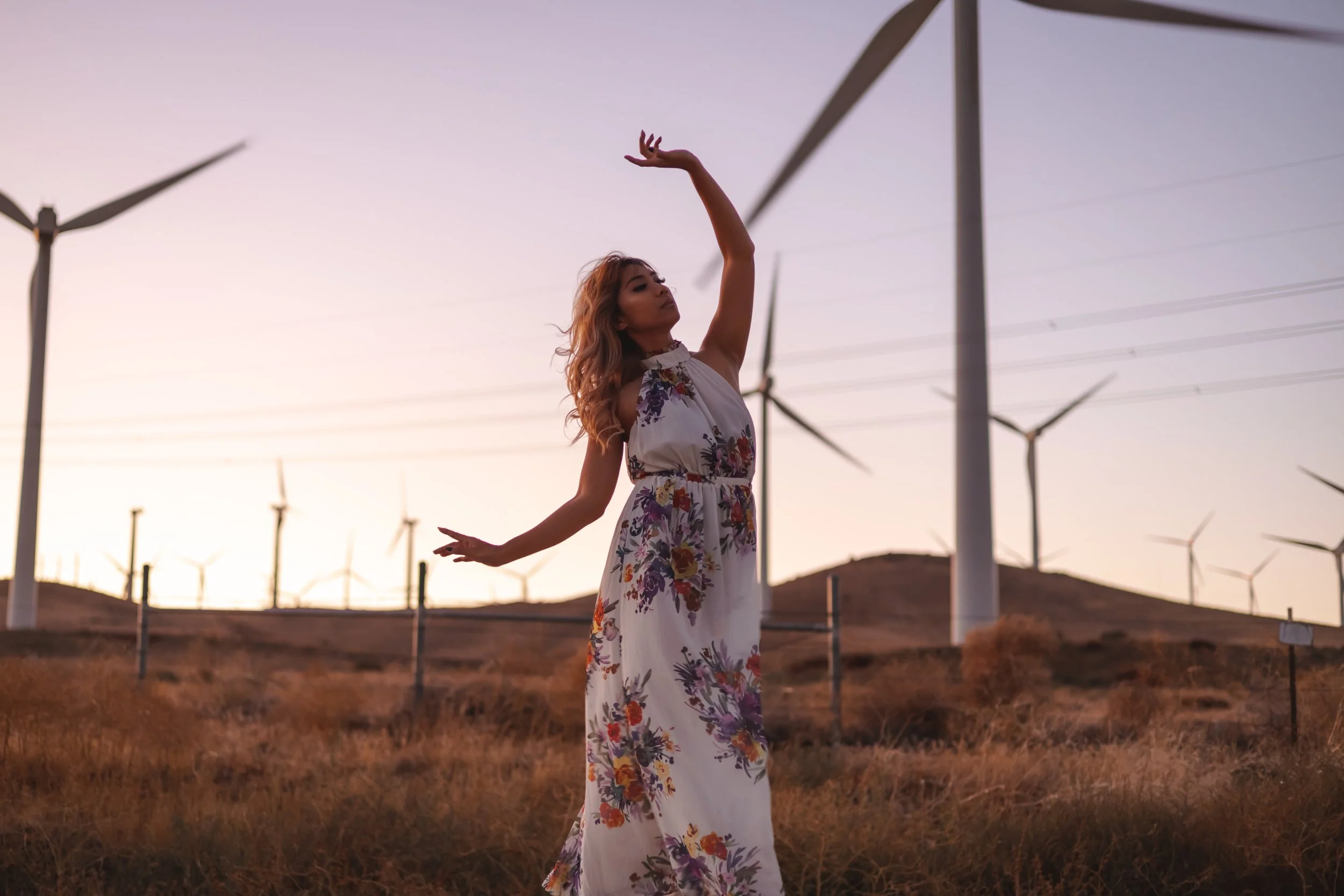 Woman in a floral dress dancing in a wind farm at sunset