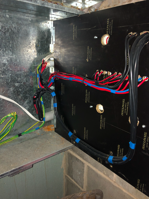 Electrical wiring inside a metal panel with organized black, red, blue, green, and yellow cables secured with blue cable ties