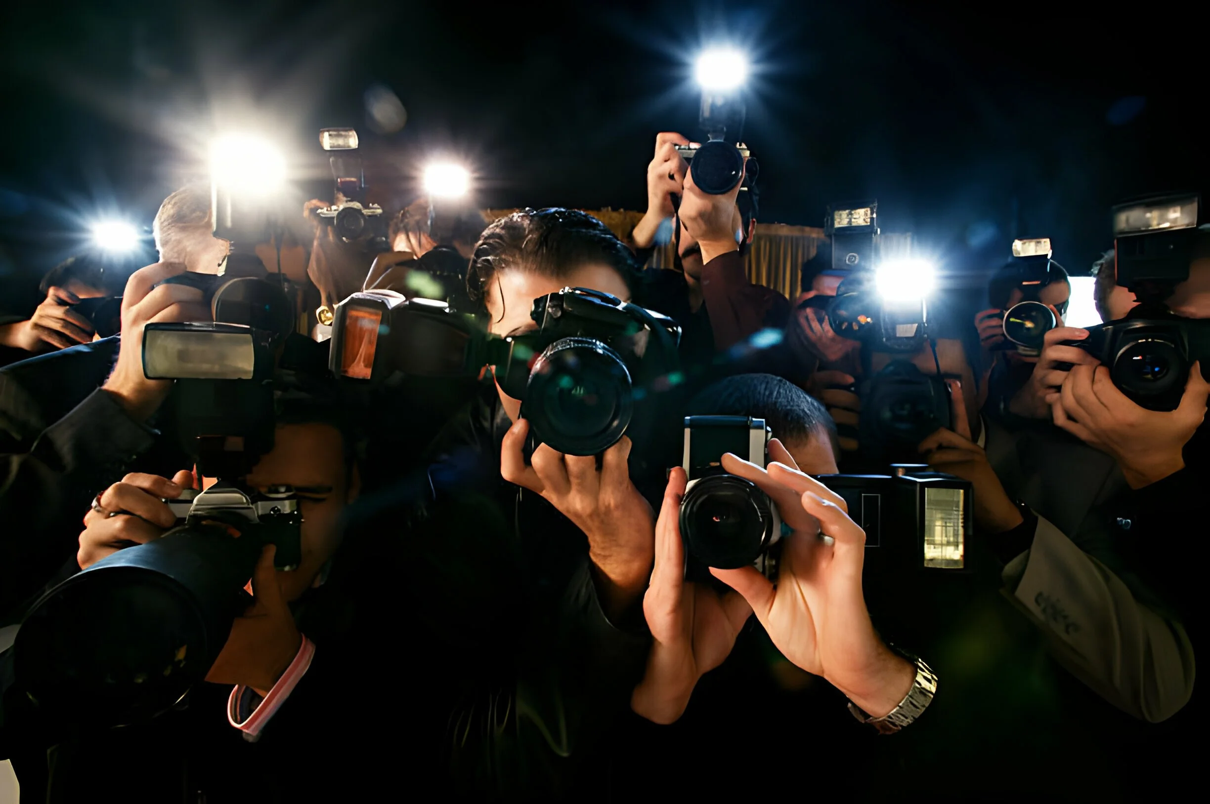 Group of photographers taking pictures at night, with camera flashes and bright lights.
