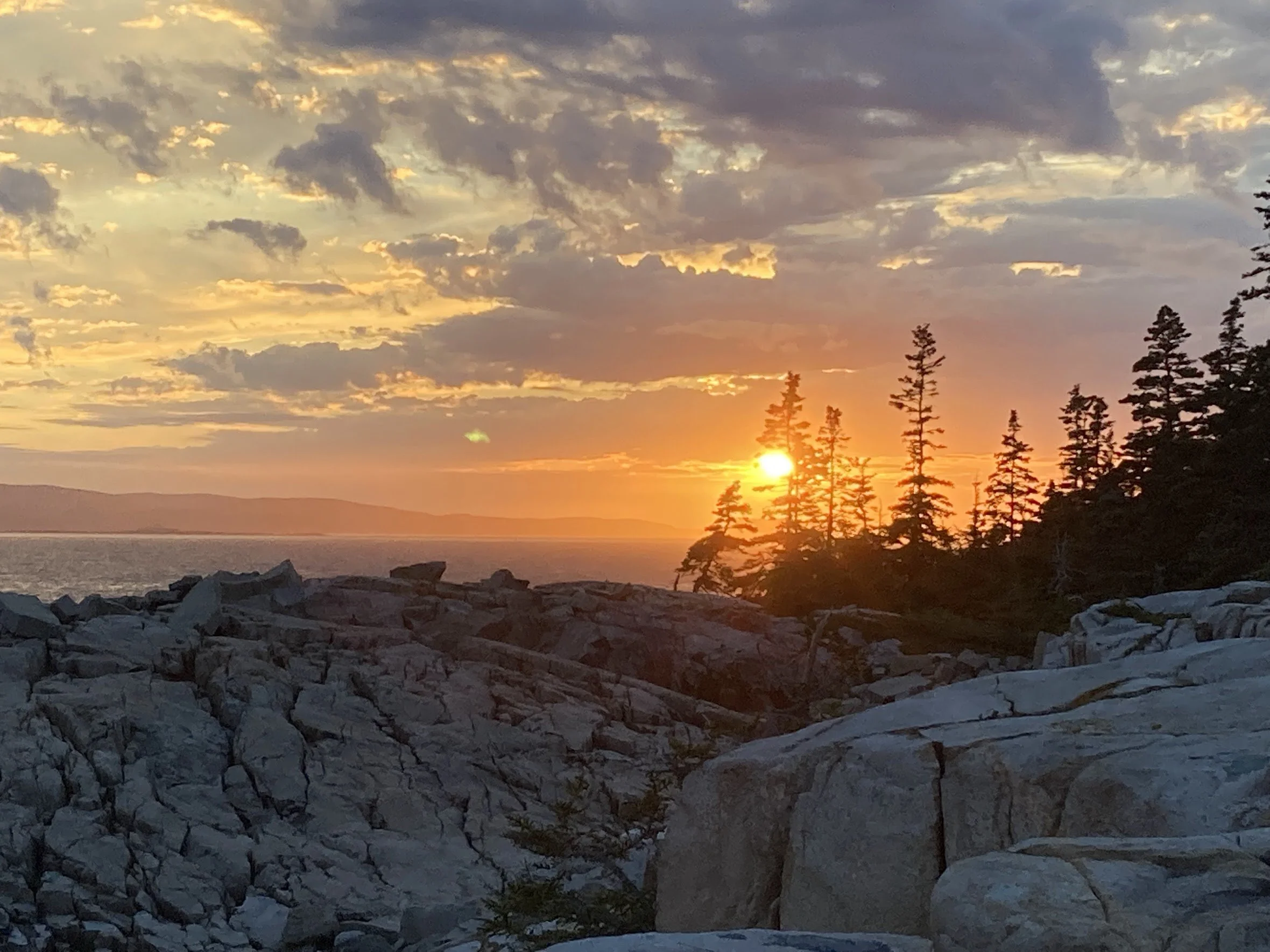 A sun setting over the water on the rocky coast of Maine