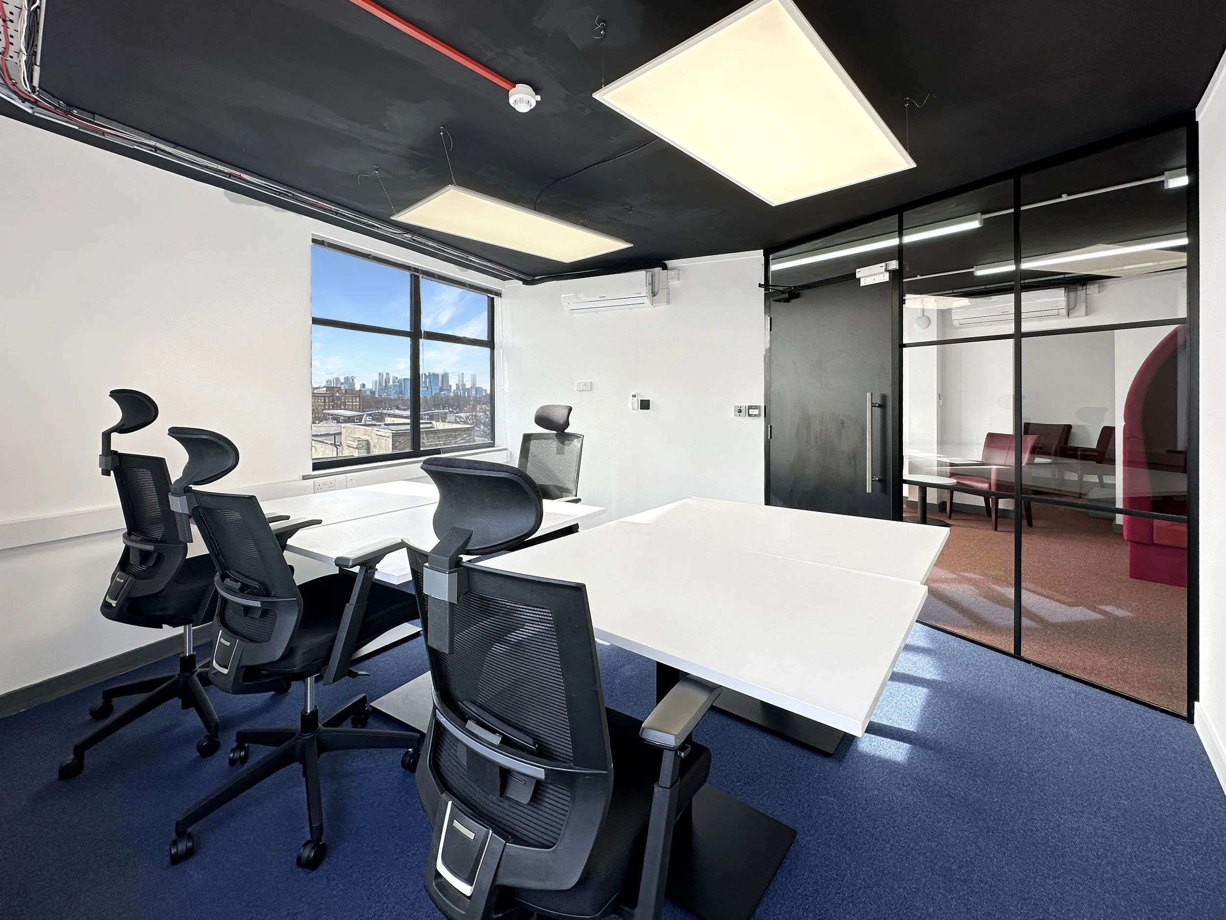 Modern office interior with ergonomic chairs, white desks, glass partition, and city view from window.