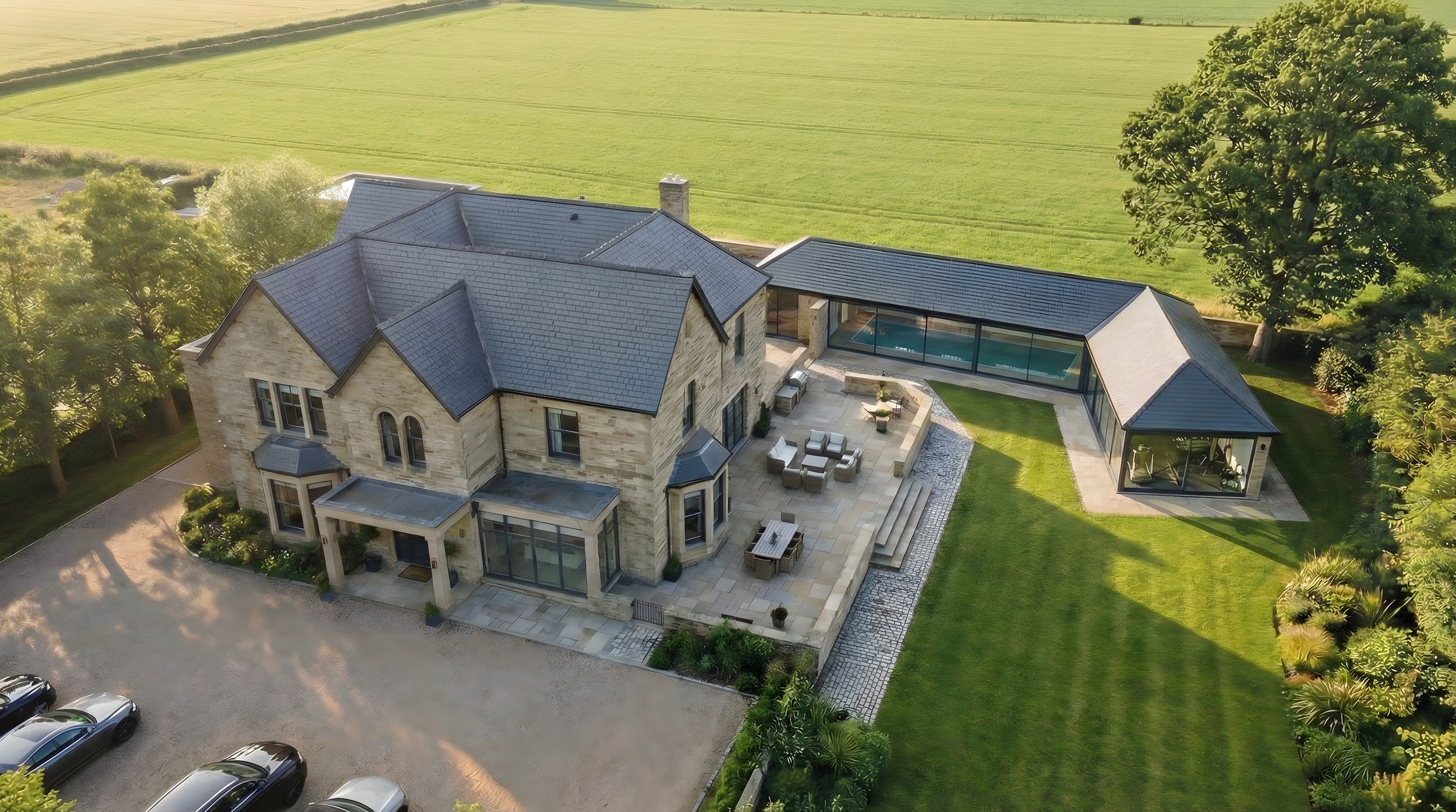 Aerial view of large stone manor house with contemporary glazed pool extension, courtyard and landscaped gardens, West Yorkshire.