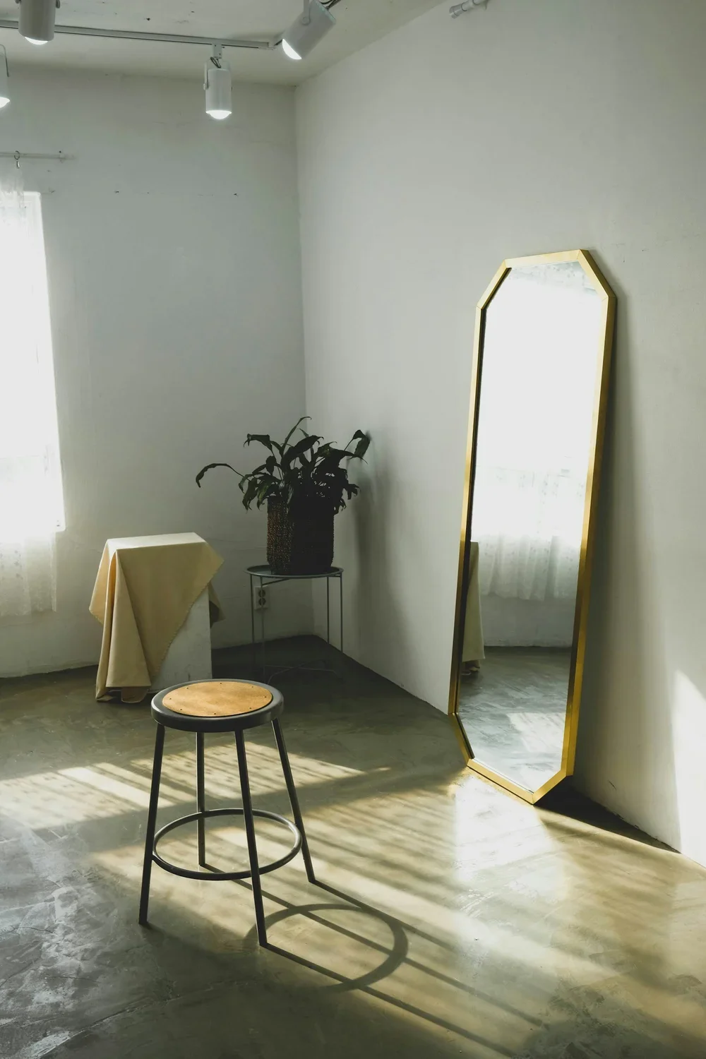full length mirror leaning up against a wall with a bar stool in front of it. No one is in the room, signifiying this is waiting for you or someone.
