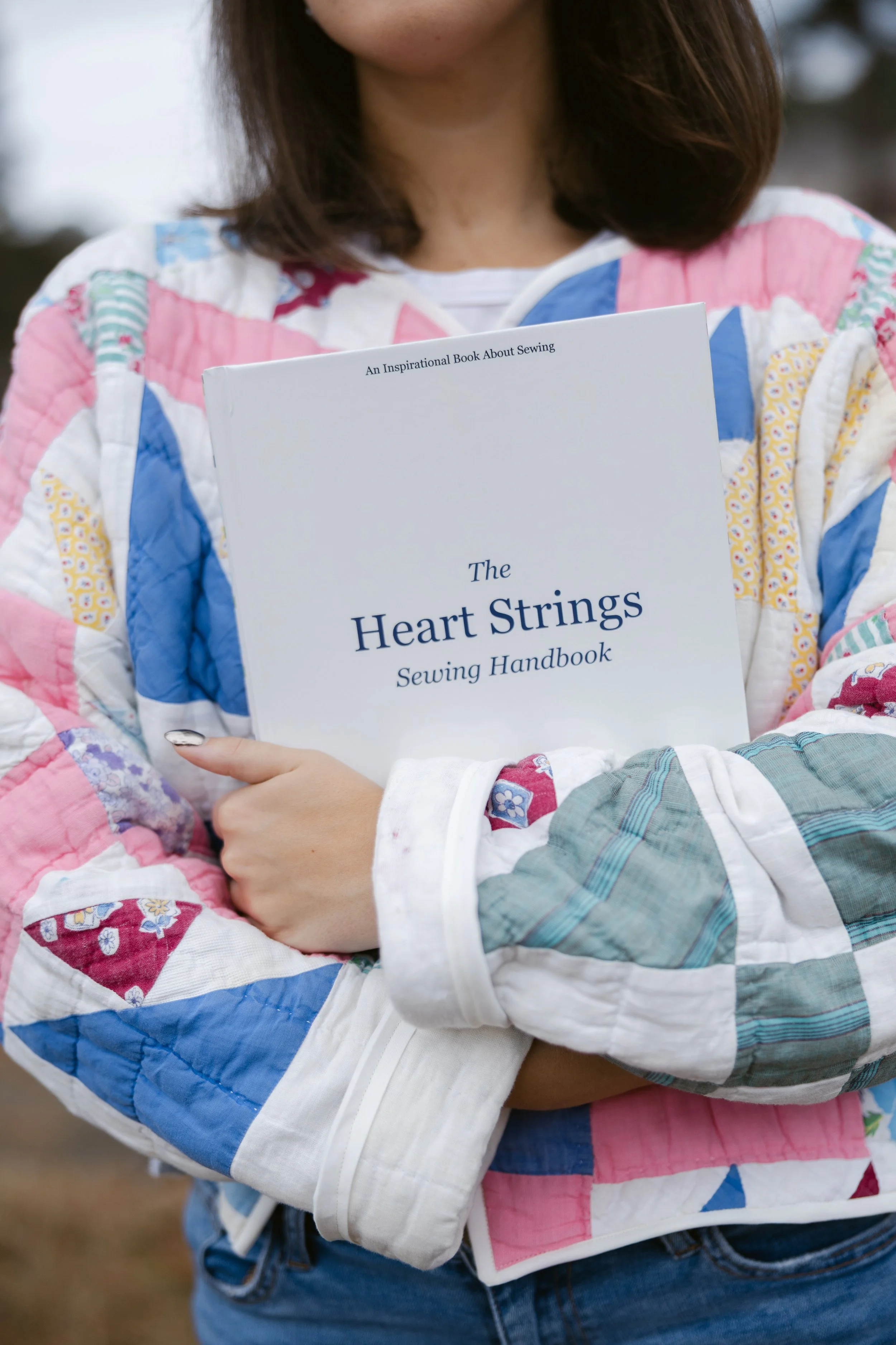 Person holding a sewing handbook titled "The Heart Strings Sewing Handbook".