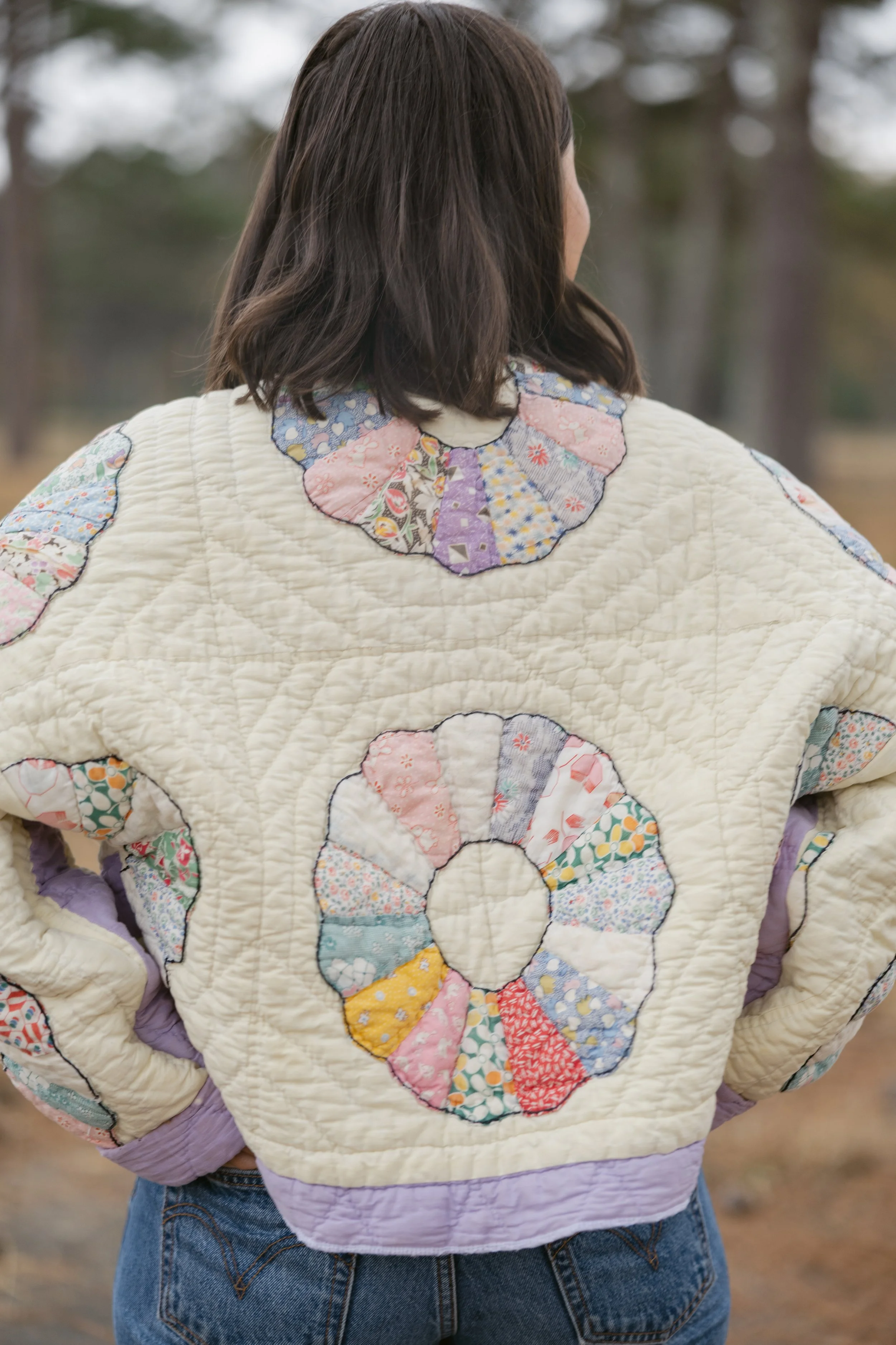 Back view of a woman wearing a quilted jacket with colorful patchwork circle designs, standing outdoors.