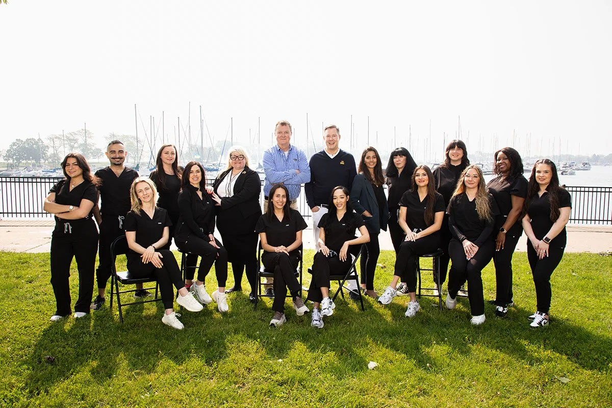 Group of people dressed in black, posing outdoors near a lake.