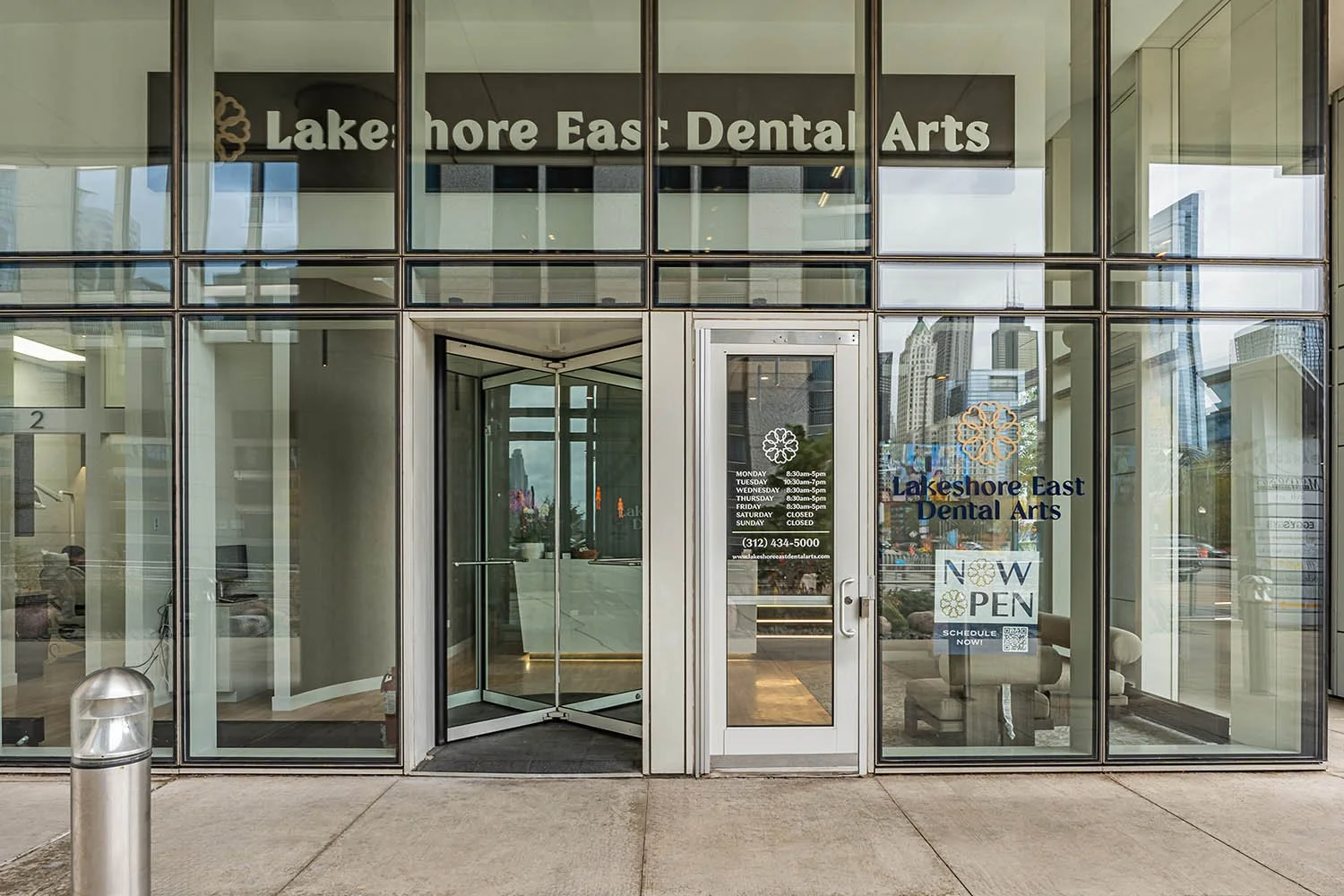 The entrance of Lakeshore East Dental Arts, a dental office with glass doors and windows. The office hours and contact information are displayed on the door, with a 'Now Open' sign indicating it is open for appointments.