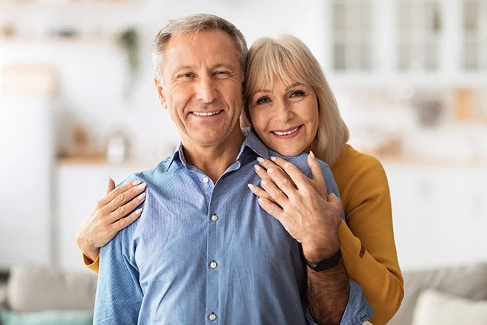 A happy elderly couple smiling and hugging in a bright, modern kitchen.