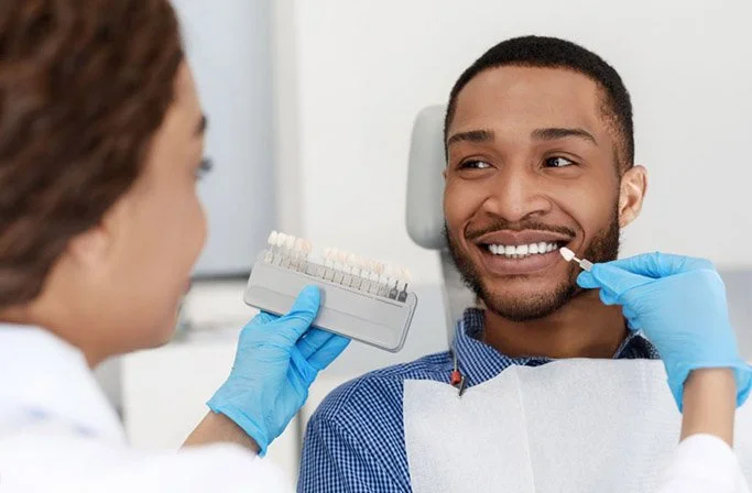 Dentist using shade guide to match color of patient's teeth during dental exam.