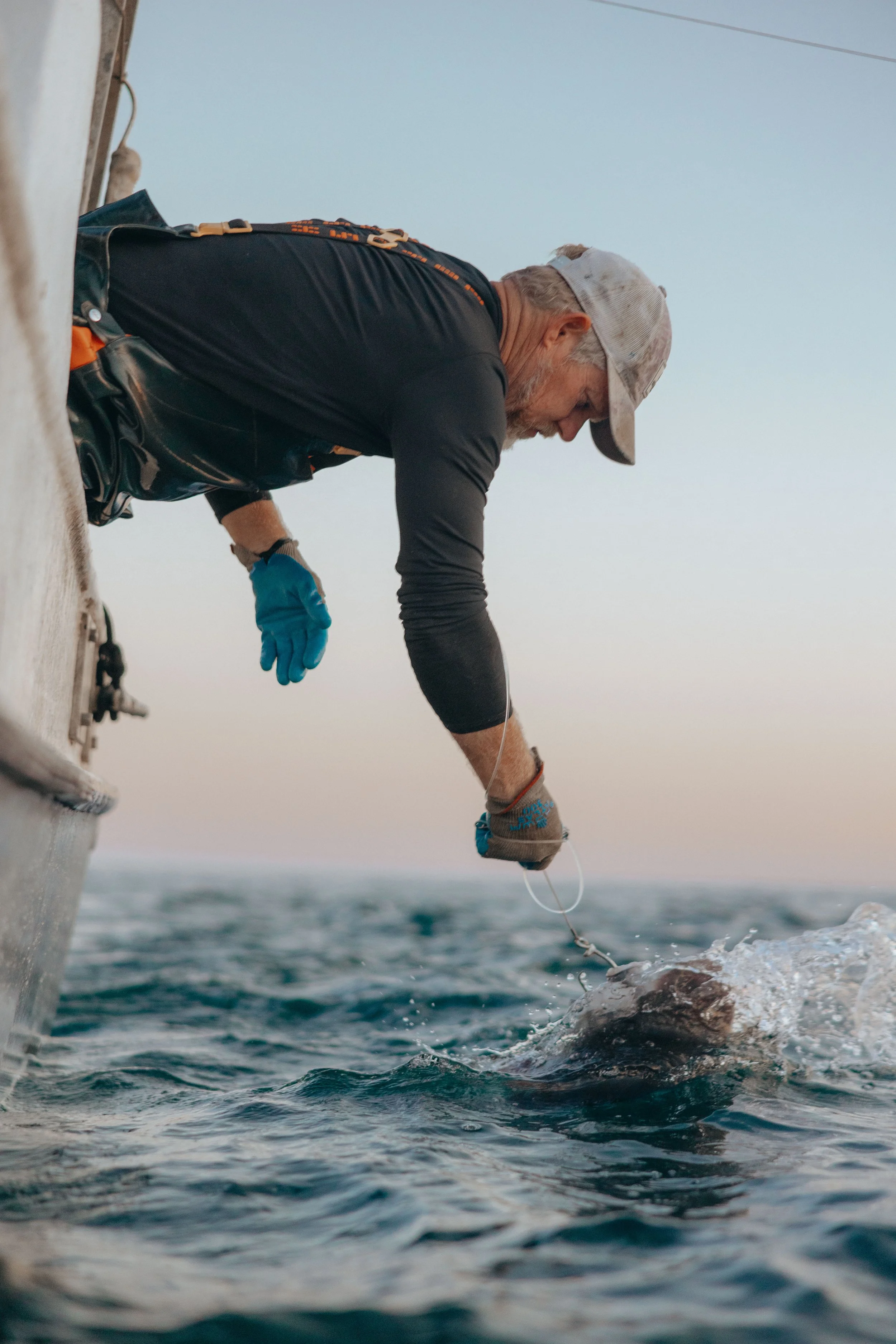 Man on boat catching fish with hook and gloves above ocean water.