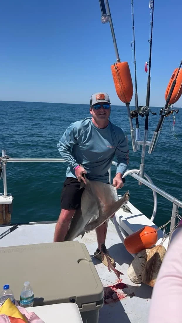 Person holding a shark on a boat with fishing rods and buoys
