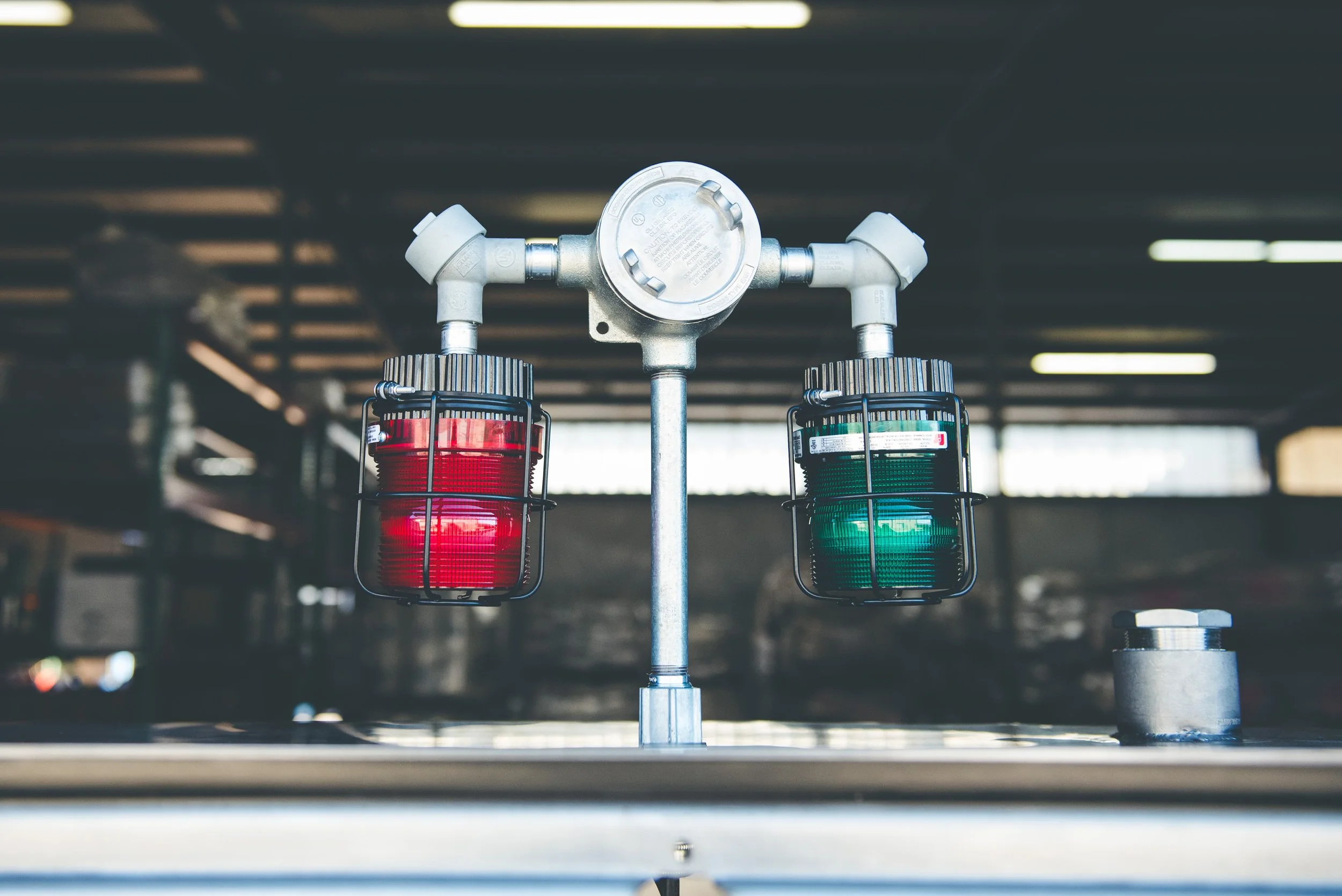 Industrial warning lights, red on the left and green on the right, mounted on a metal pipe in a factory or warehouse setting.