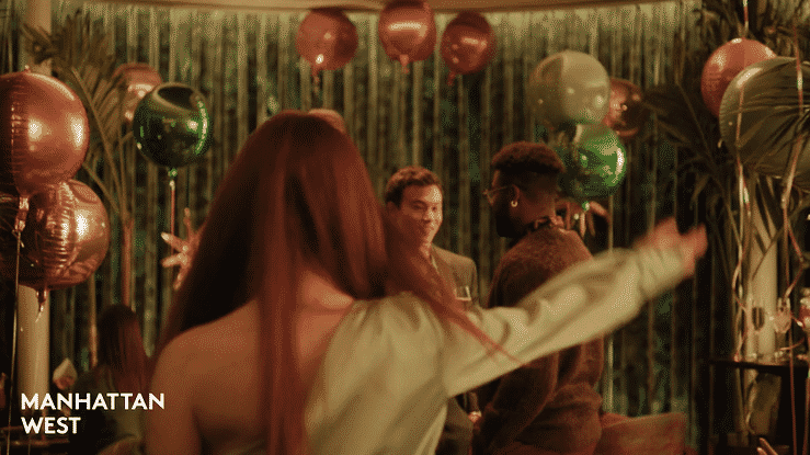 People dancing and socializing at a party decorated with metallic balloons and green foliage in the background.