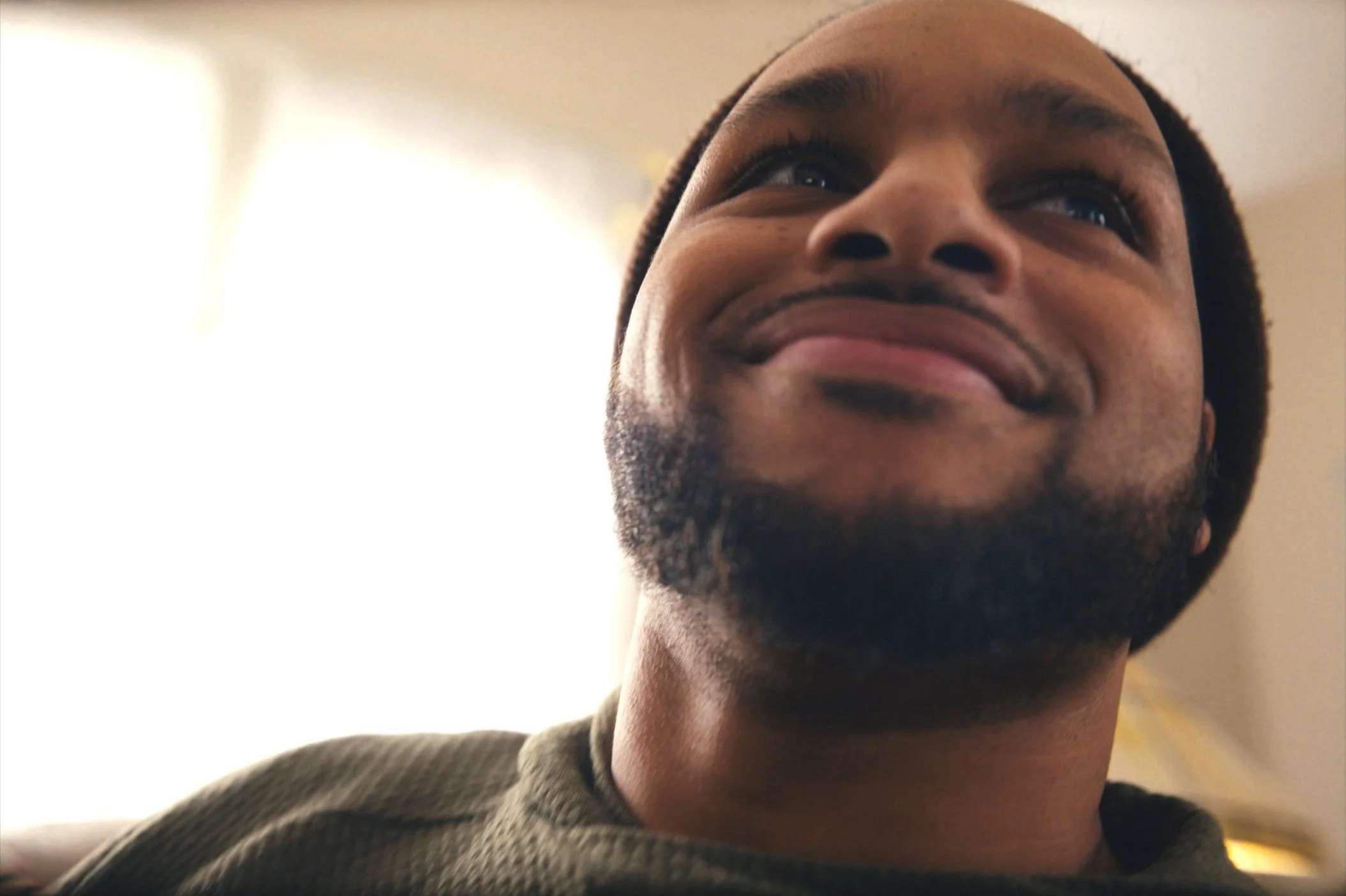 Close-up of a smiling man with a beard, wearing a beanie, looking upwards.