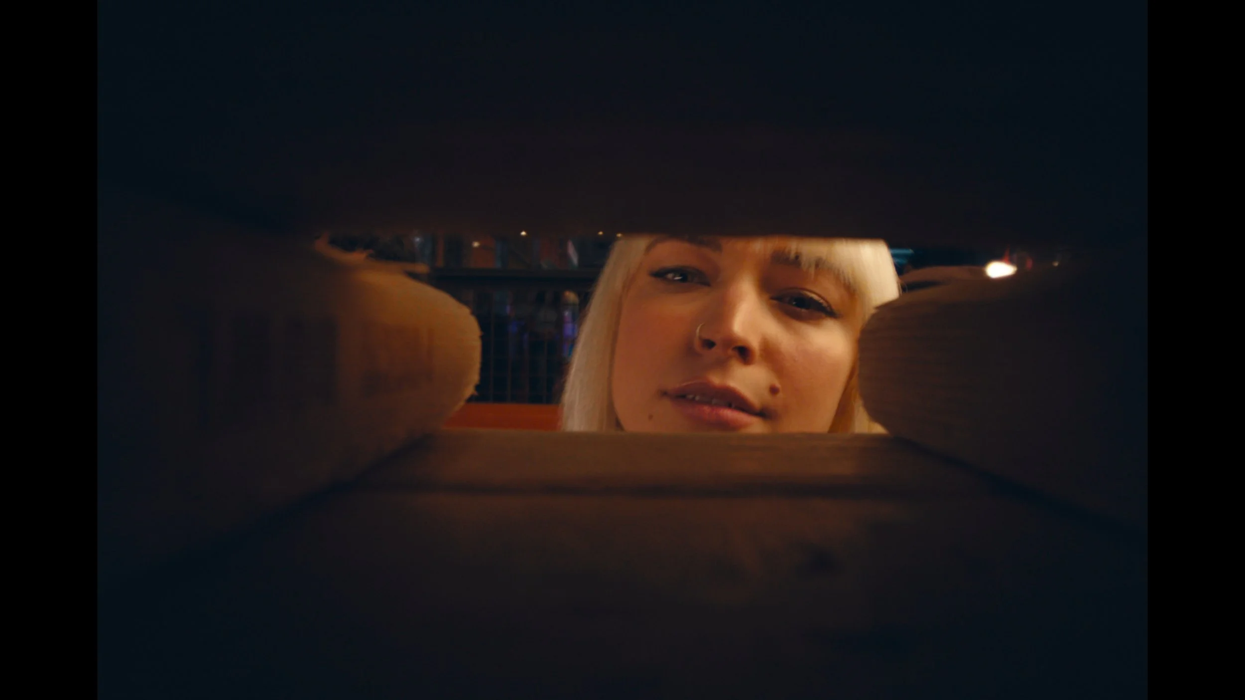 A woman with blonde hair and a nose ring looks down into an open drawer or compartment, smiling slightly.