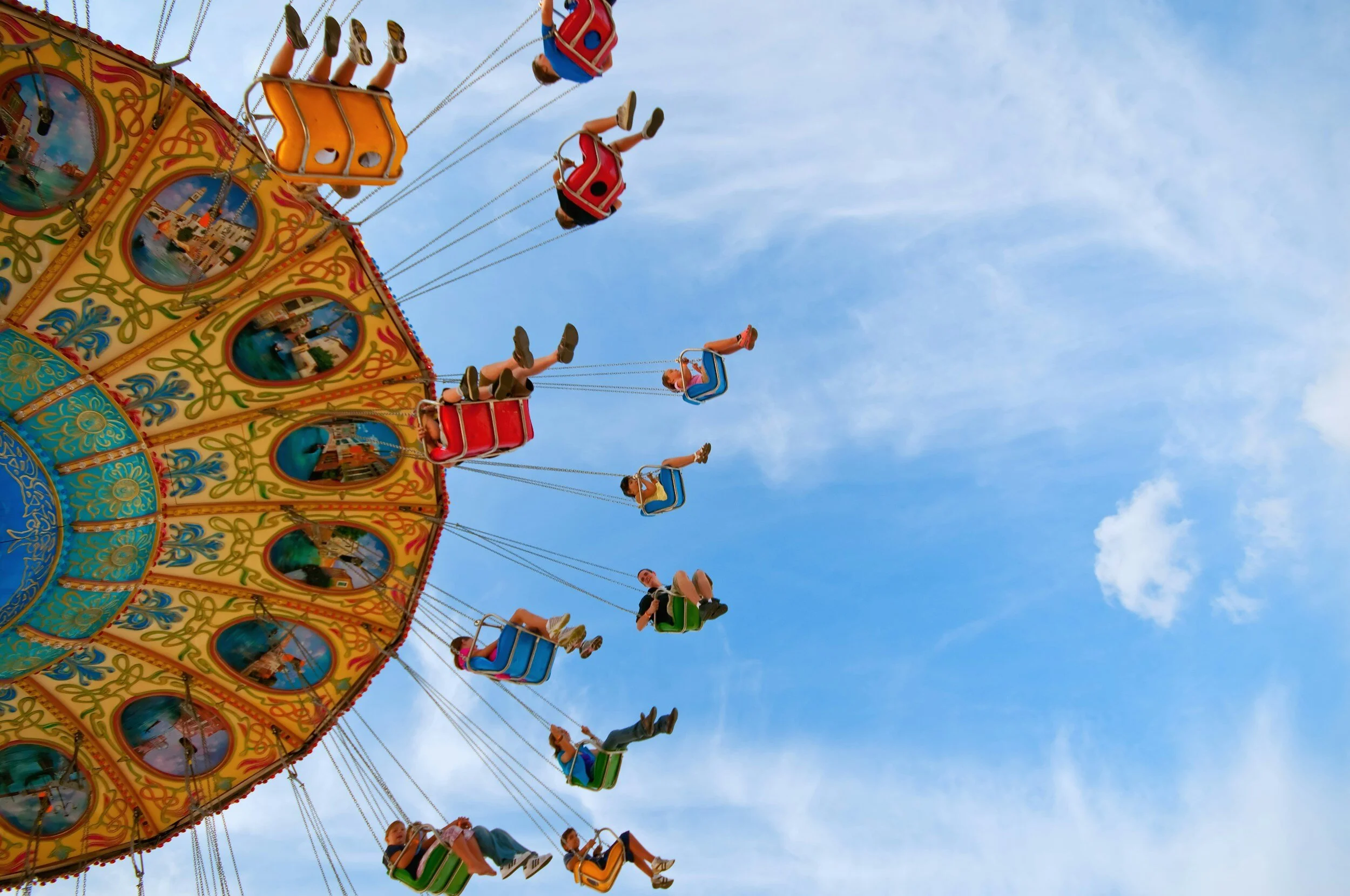 People enjoying a colorful swing carousel ride against a blue sky with clouds.