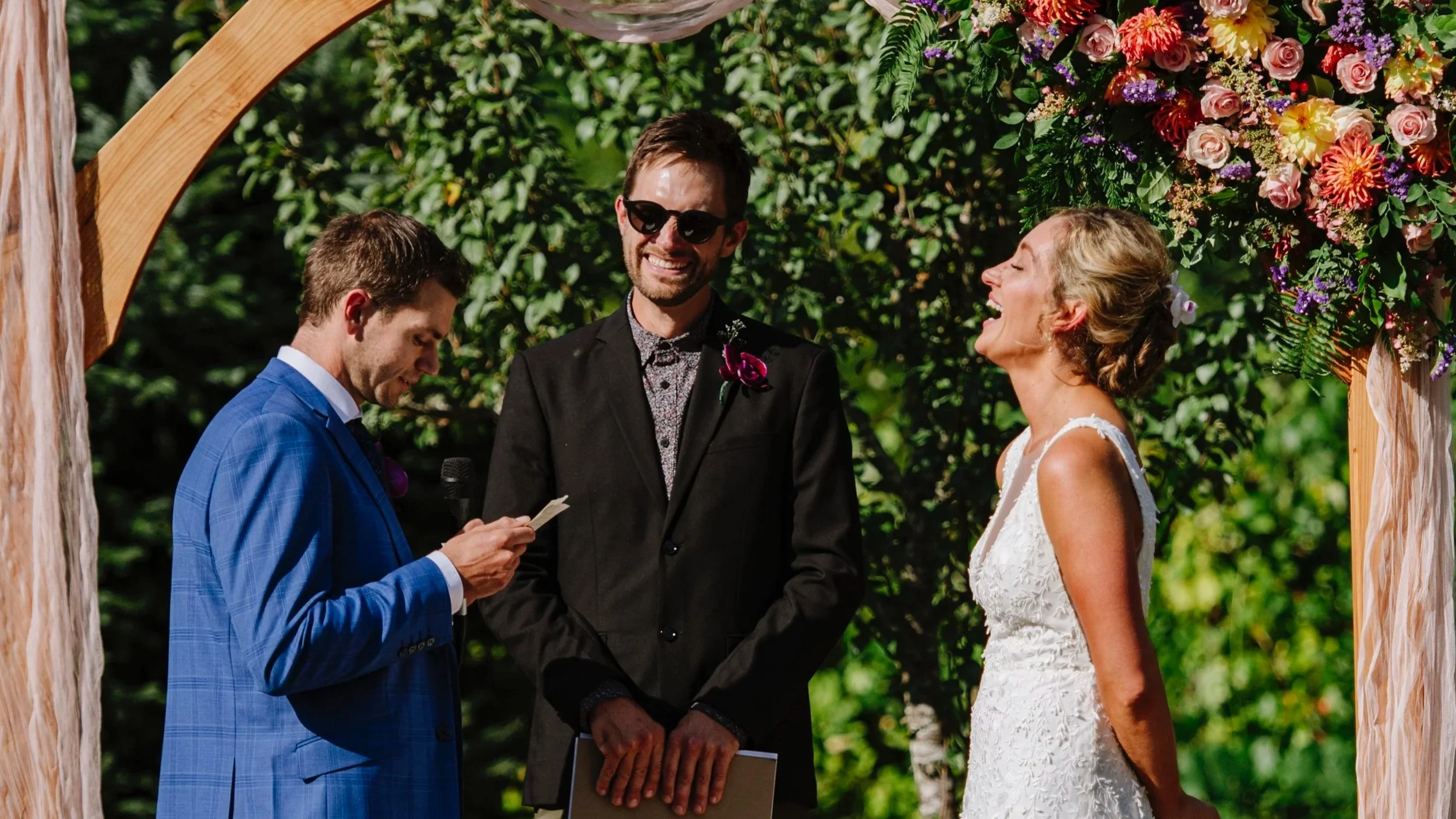 Bride and groom share a moment of laughter under a rustic wood altar.