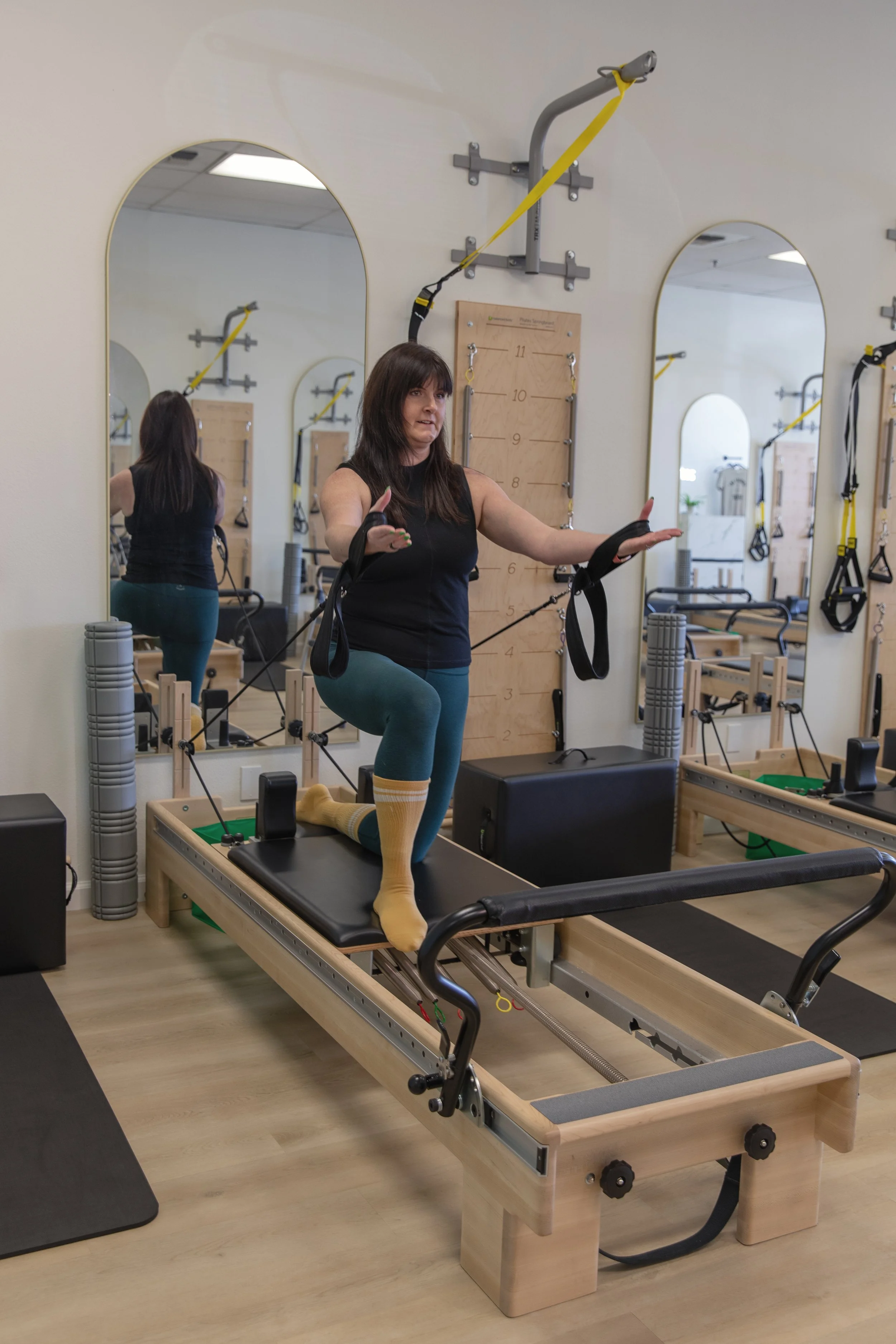Woman performing physical therapy exercise on a reformer machine with straps in a rehab or fitness studio.