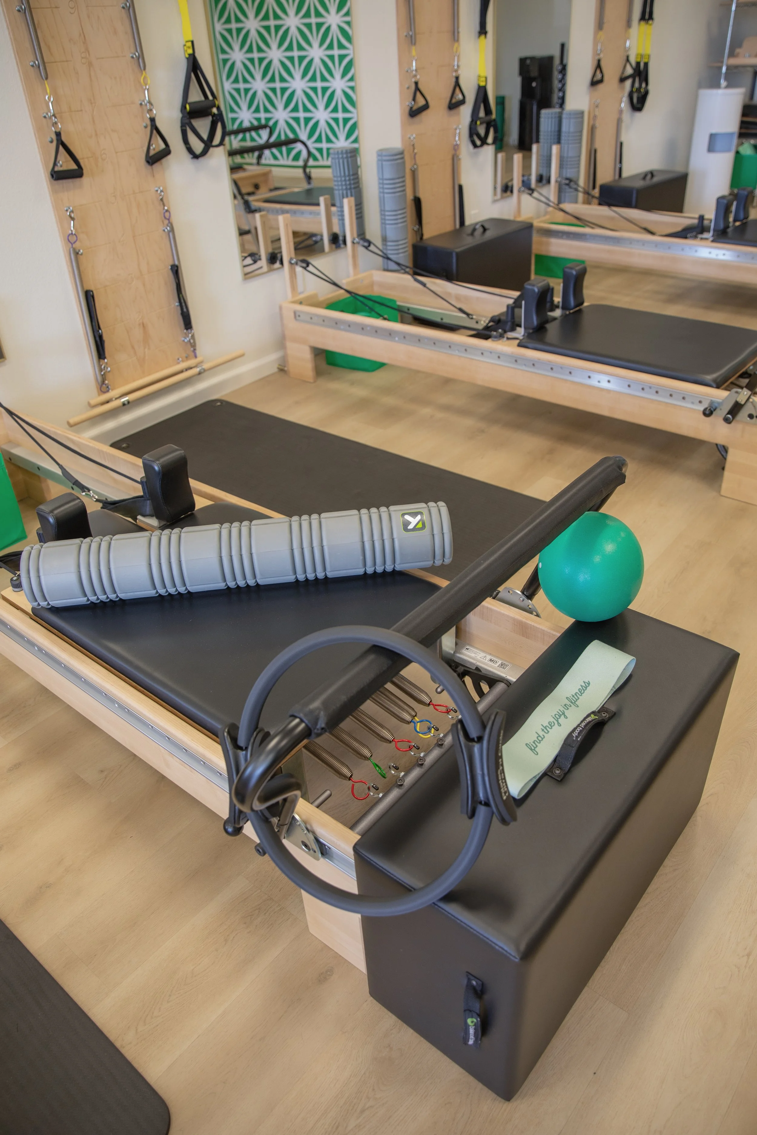 Fitness studio with Pilates reformers, yoga mats, foam rollers, resistance bands, and TRX suspension straps.