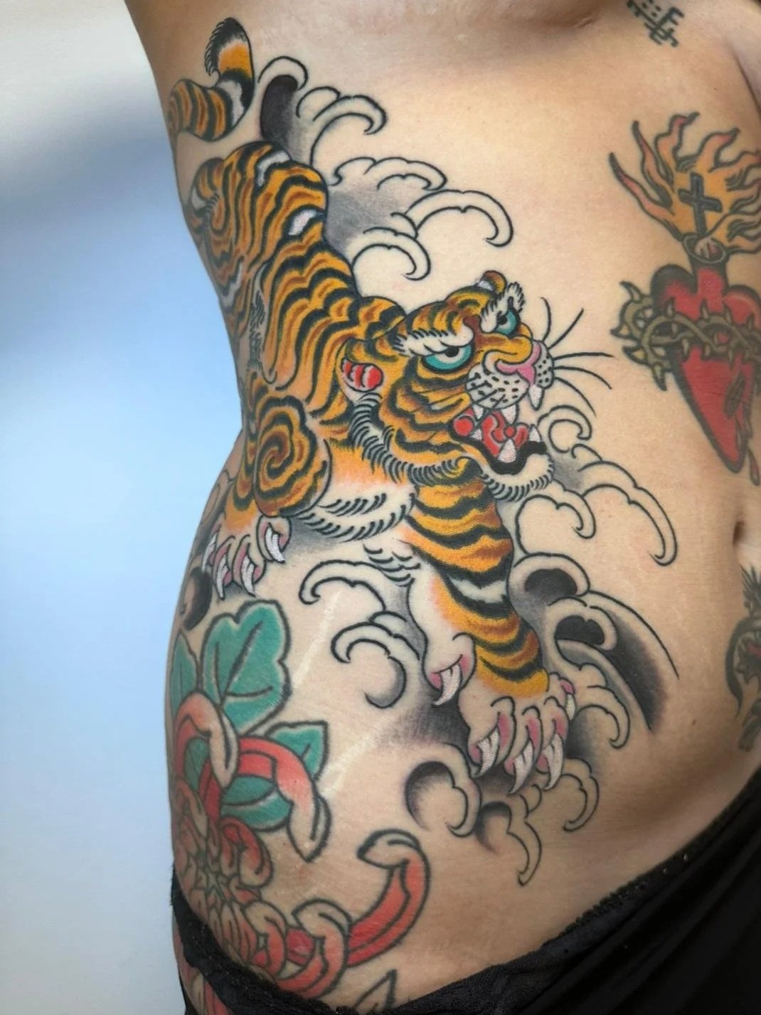 Tattoo of a traditional Japanese style tiger surrounded by clouds and foliage on a person's side and torso.
