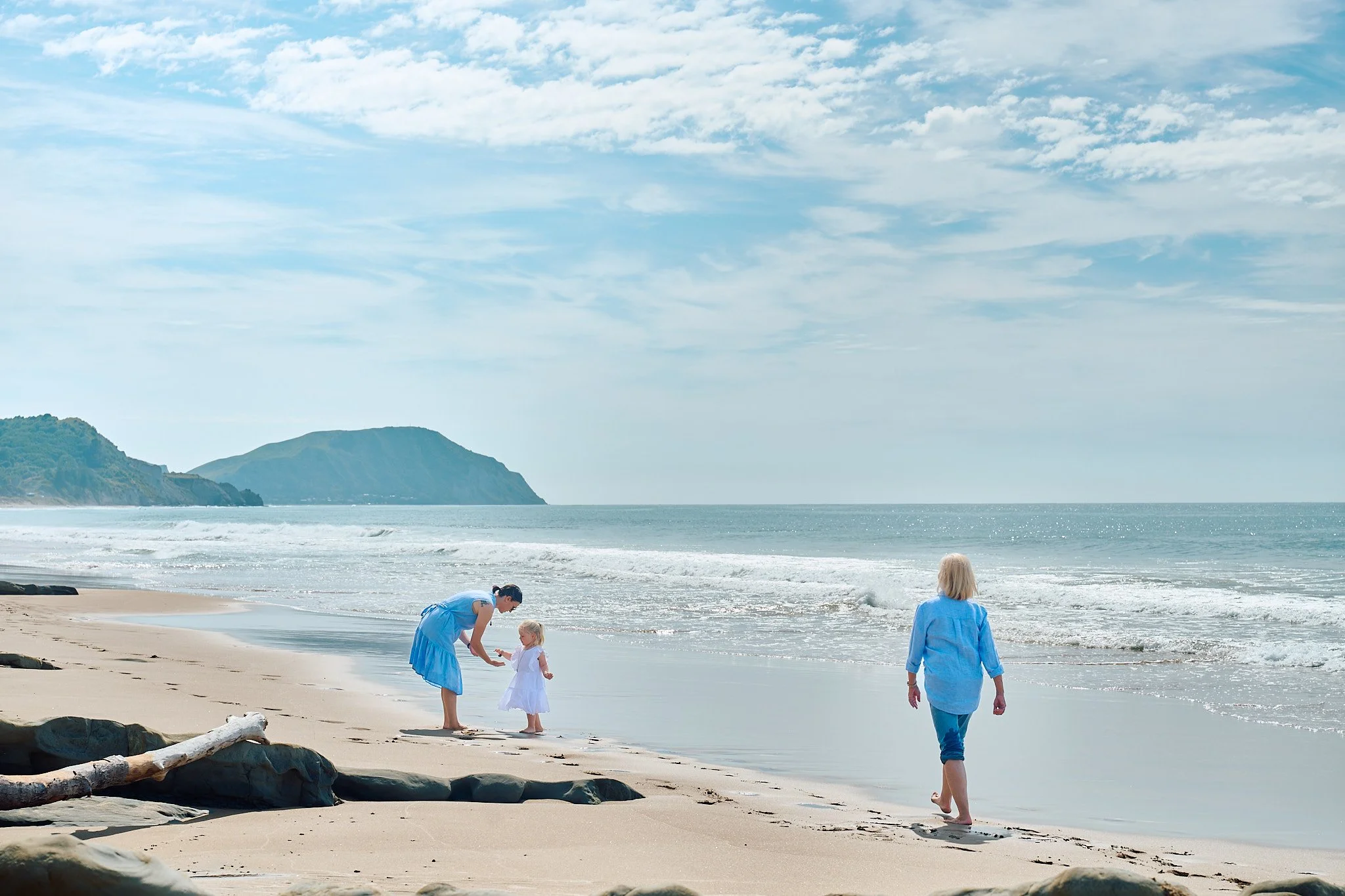 People walking on a beach by the sea with mountains in the background.