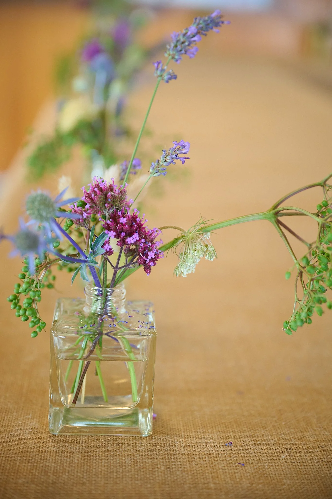 Wildflowers in a small square glass vase on a burlap tablecloth.